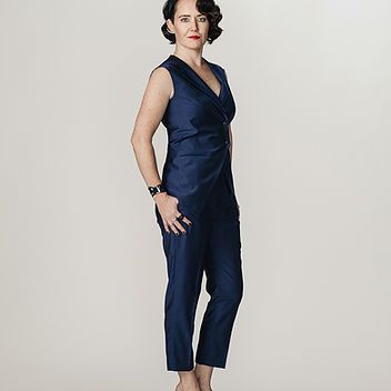 A woman in a blue jumpsuit is standing in front of a white background.
