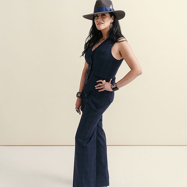 A woman wearing a hat and a vest is standing in front of a wall