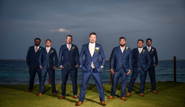 The groom and his groomsmen are posing for a picture in front of the ocean.