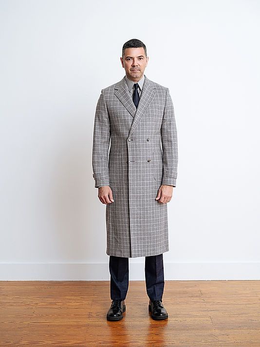 A man wearing a long coat and tie is standing on a wooden floor.