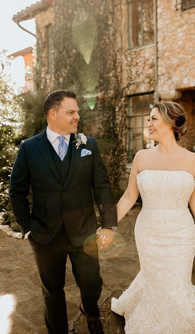 A bride and groom are holding hands and smiling while walking in front of a building.
