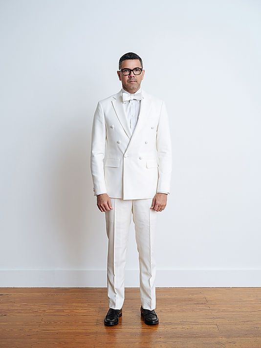 A man in a white suit and bow tie is standing on a wooden floor.