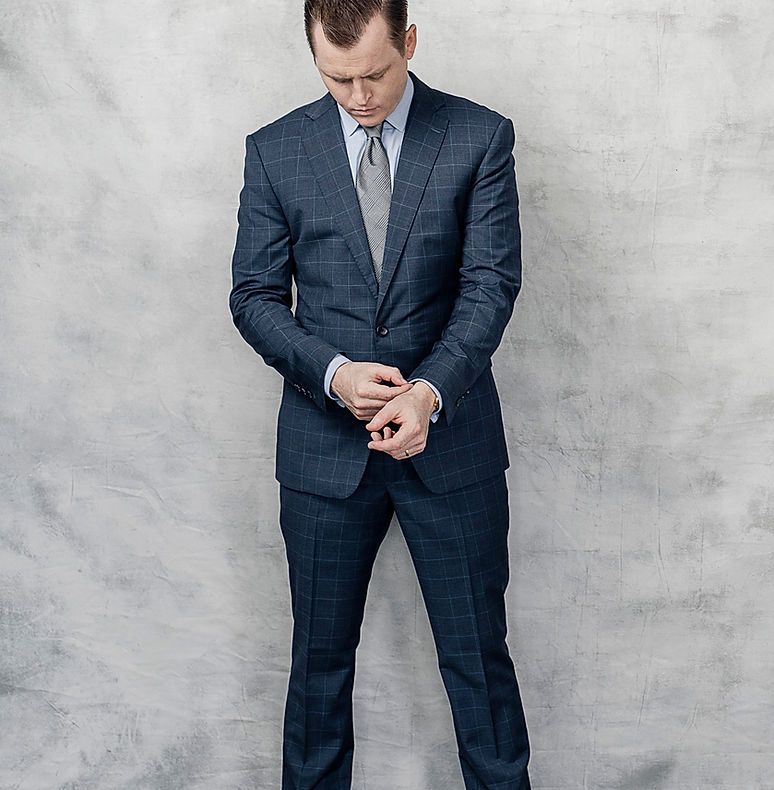 A man in a suit and tie is standing in front of a wall