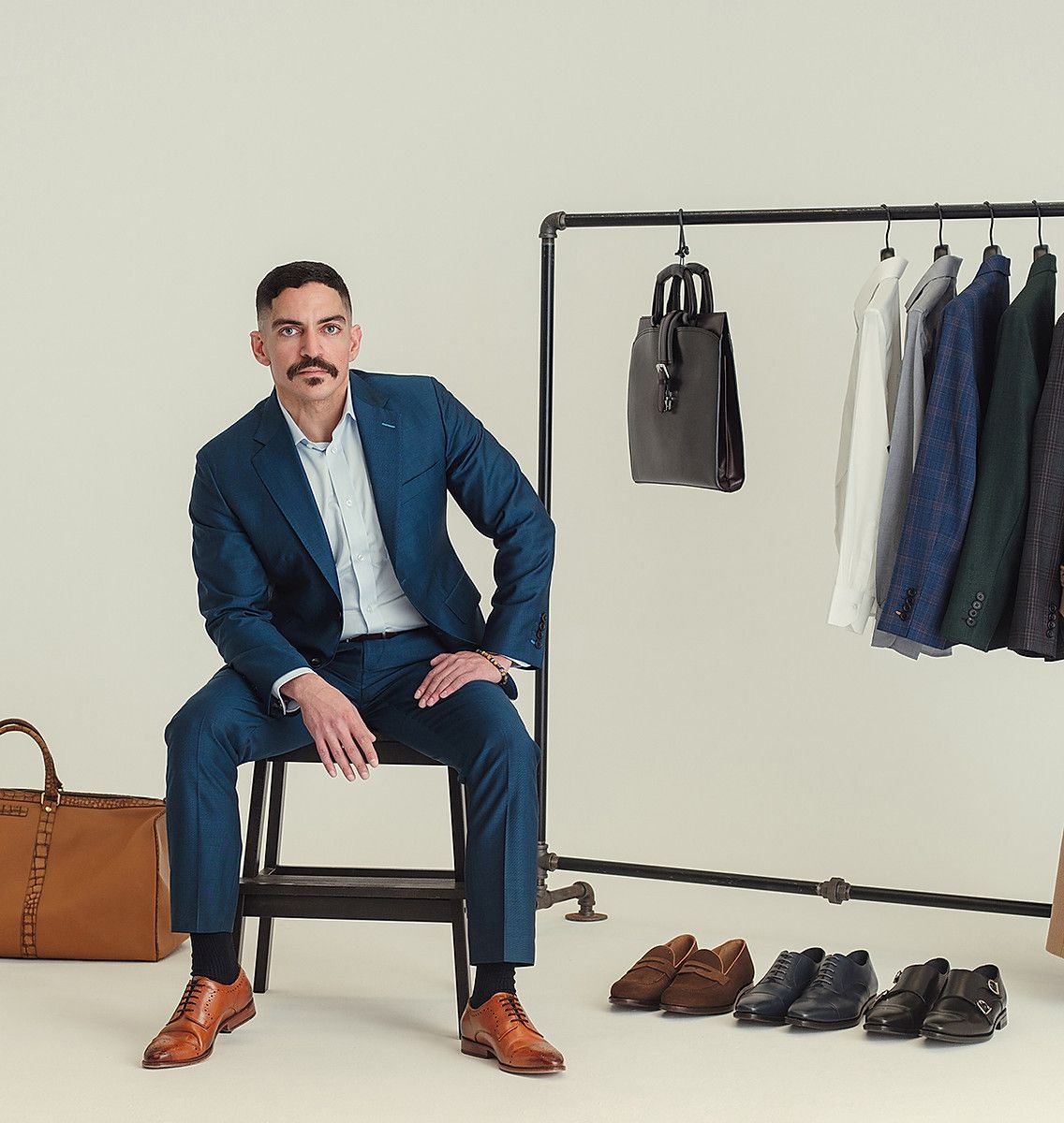 A man in a suit is sitting on a chair in front of a rack of clothes.