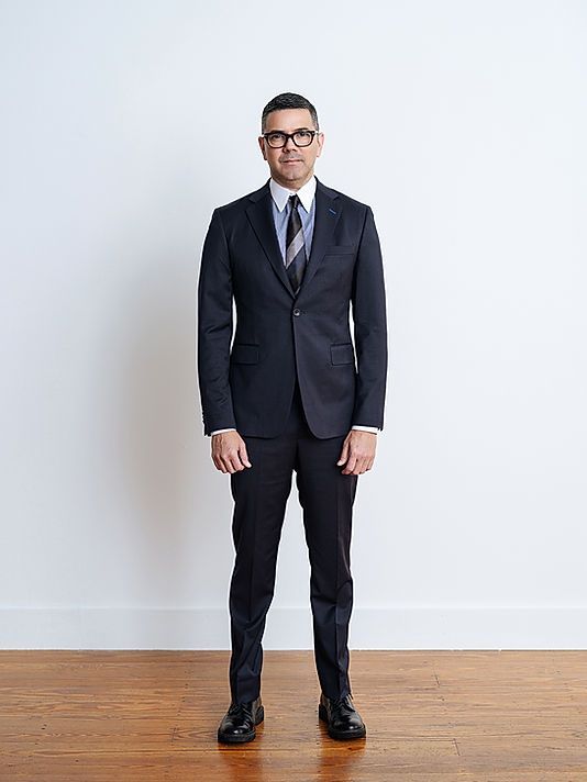 A man in a suit and tie is standing in front of a white wall.