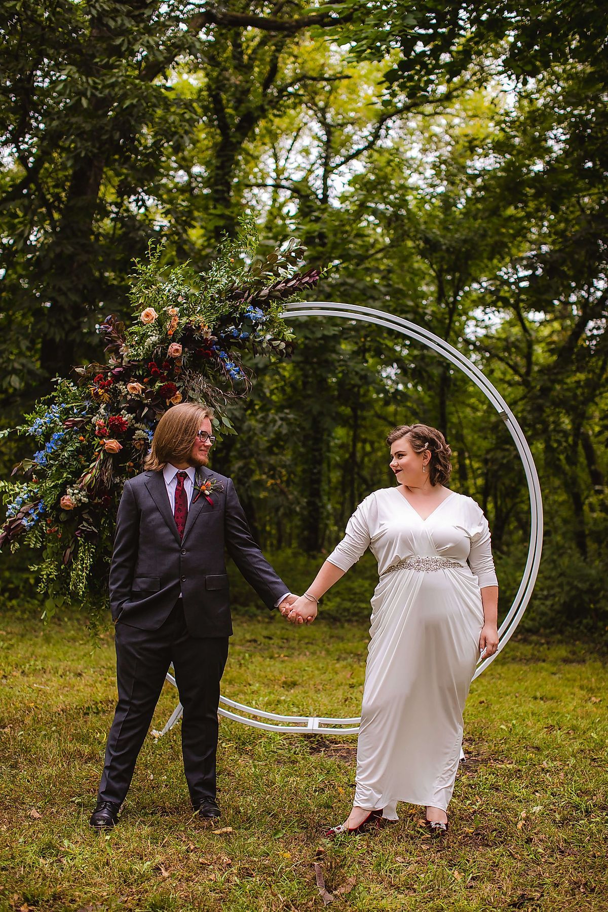 A bride and groom are holding hands in front of a floral arch.