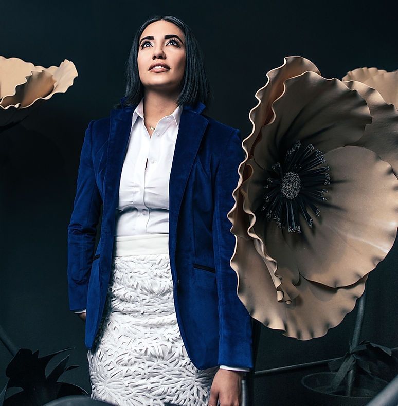A woman in a blue jacket and white skirt is standing in front of large flowers