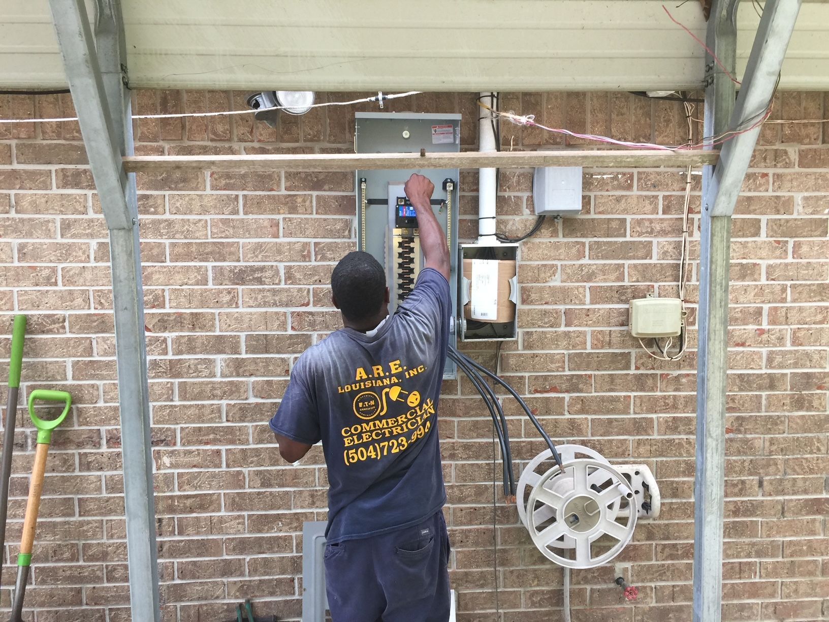 A Man Is Working on An Electrical Box on A Brick Wall.