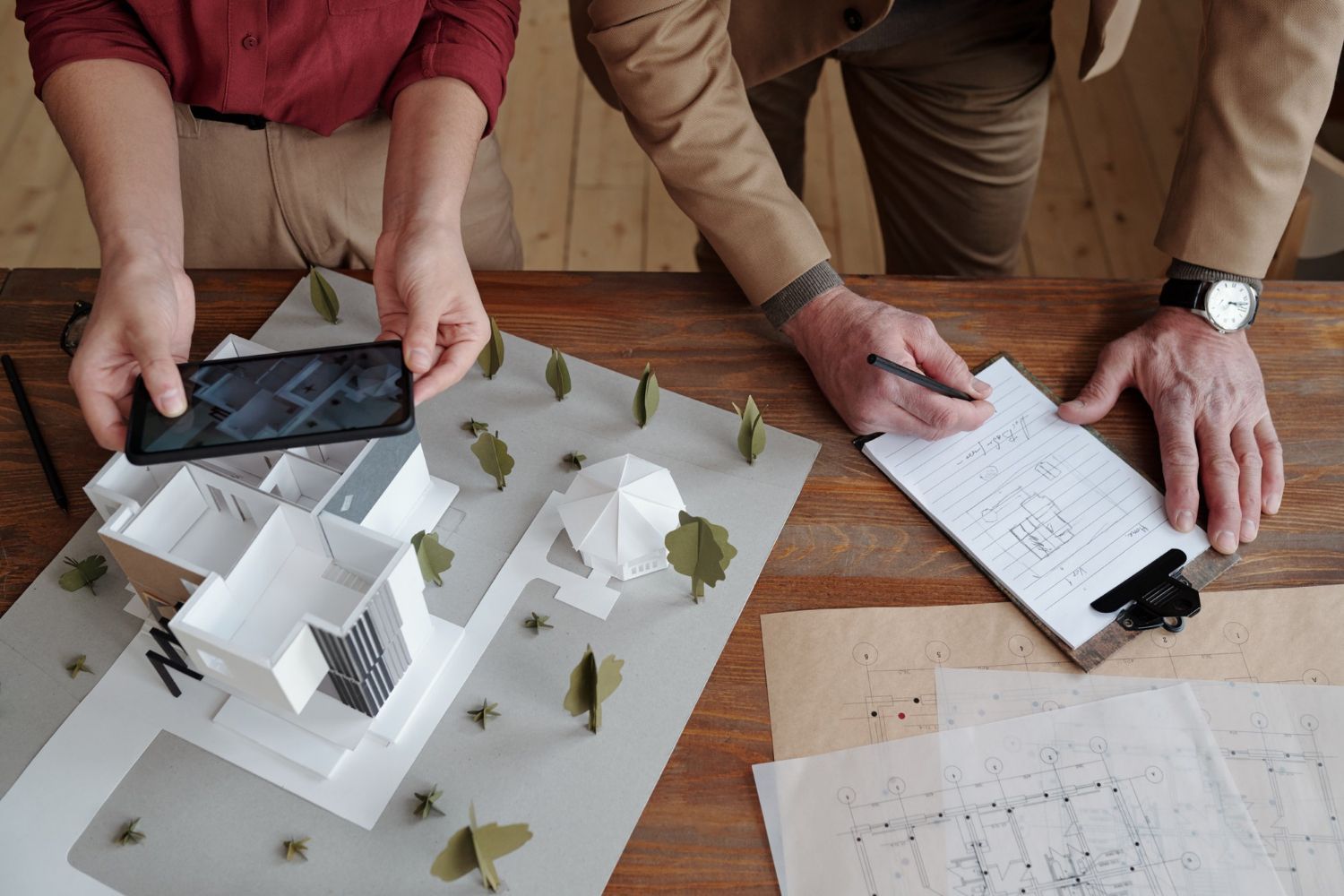 A man is taking a picture of a model house with a cell phone.