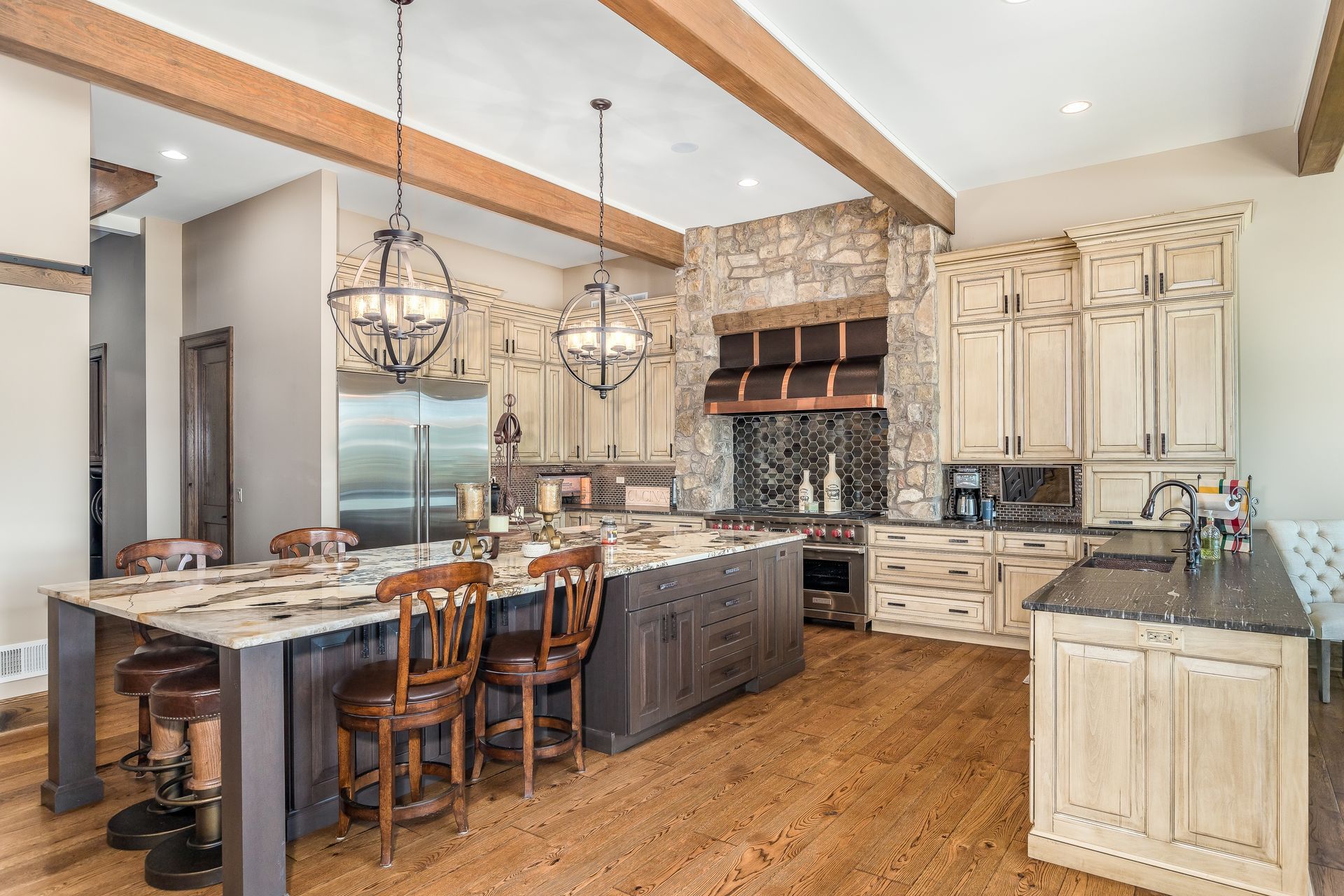 Rustic kitchen with wooden floors, island with seating, and stone range hood.