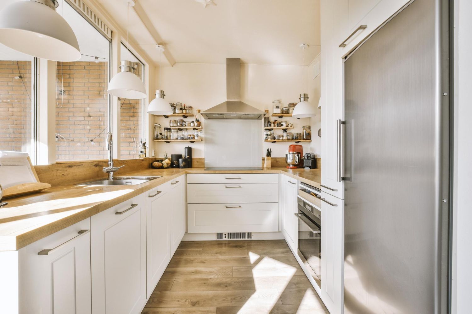 White kitchen with light wooden countertops, stainless steel appliances, and pendant lights.