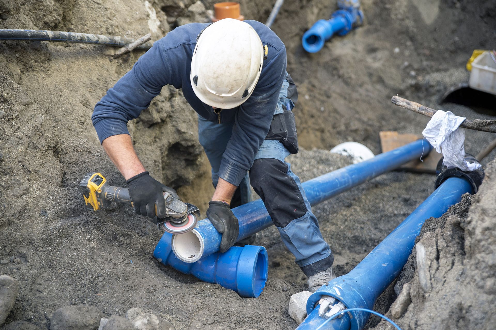 A man is working on a pipe in the dirt.