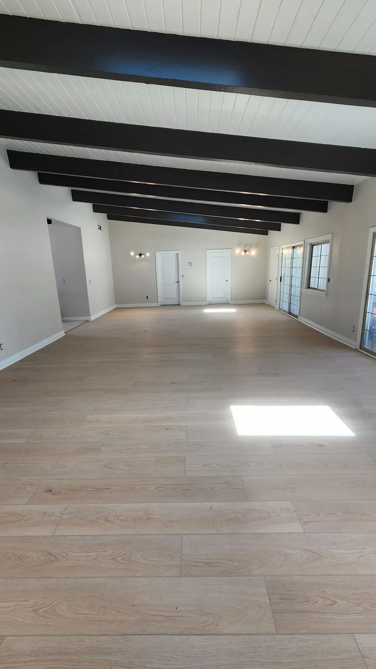 A large empty room with wooden floors and black beams.