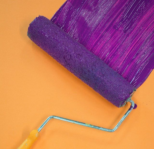 A purple paint roller is being used to paint a wall.