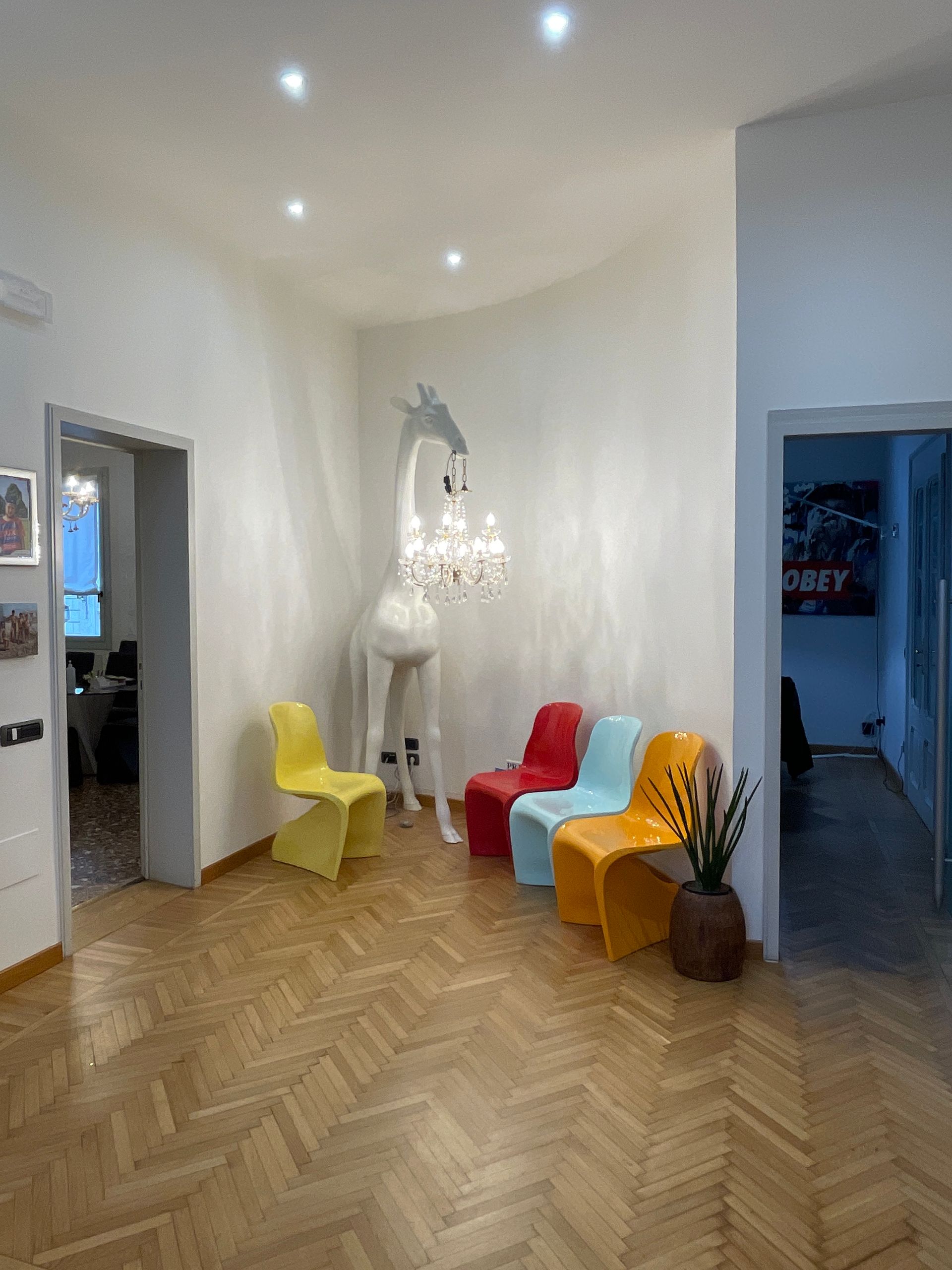 Una lampada a forma di giraffa è appesa sopra delle sedie colorate in una stanza con pavimento in legno.