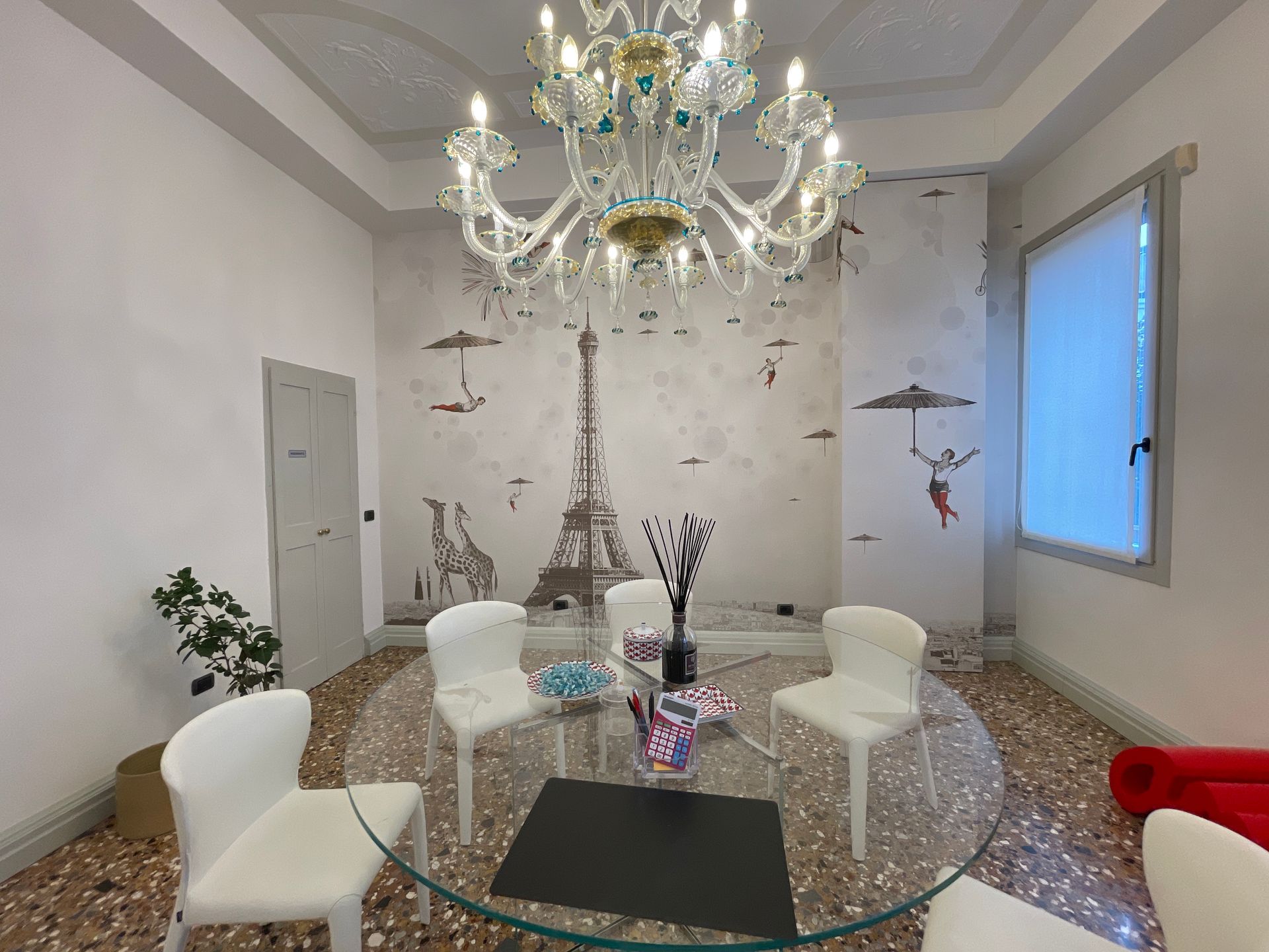 Tavolo rotondo in vetro con sedie bianche, lampadario e decorazione murale raffigurante la Torre Eiffel.