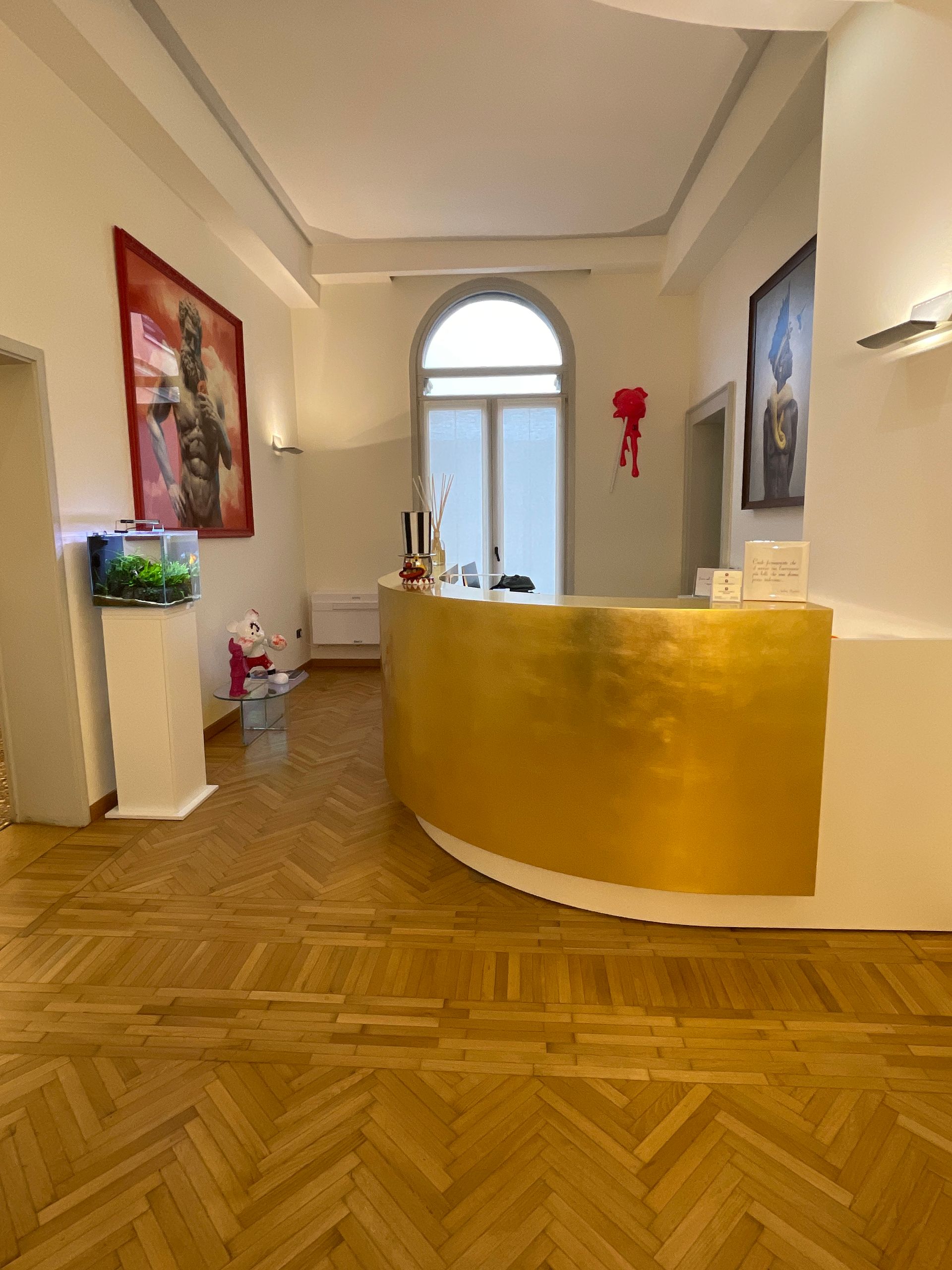 Area reception con bancone curvo color oro, acquario, opere d'arte e pavimento in parquet.