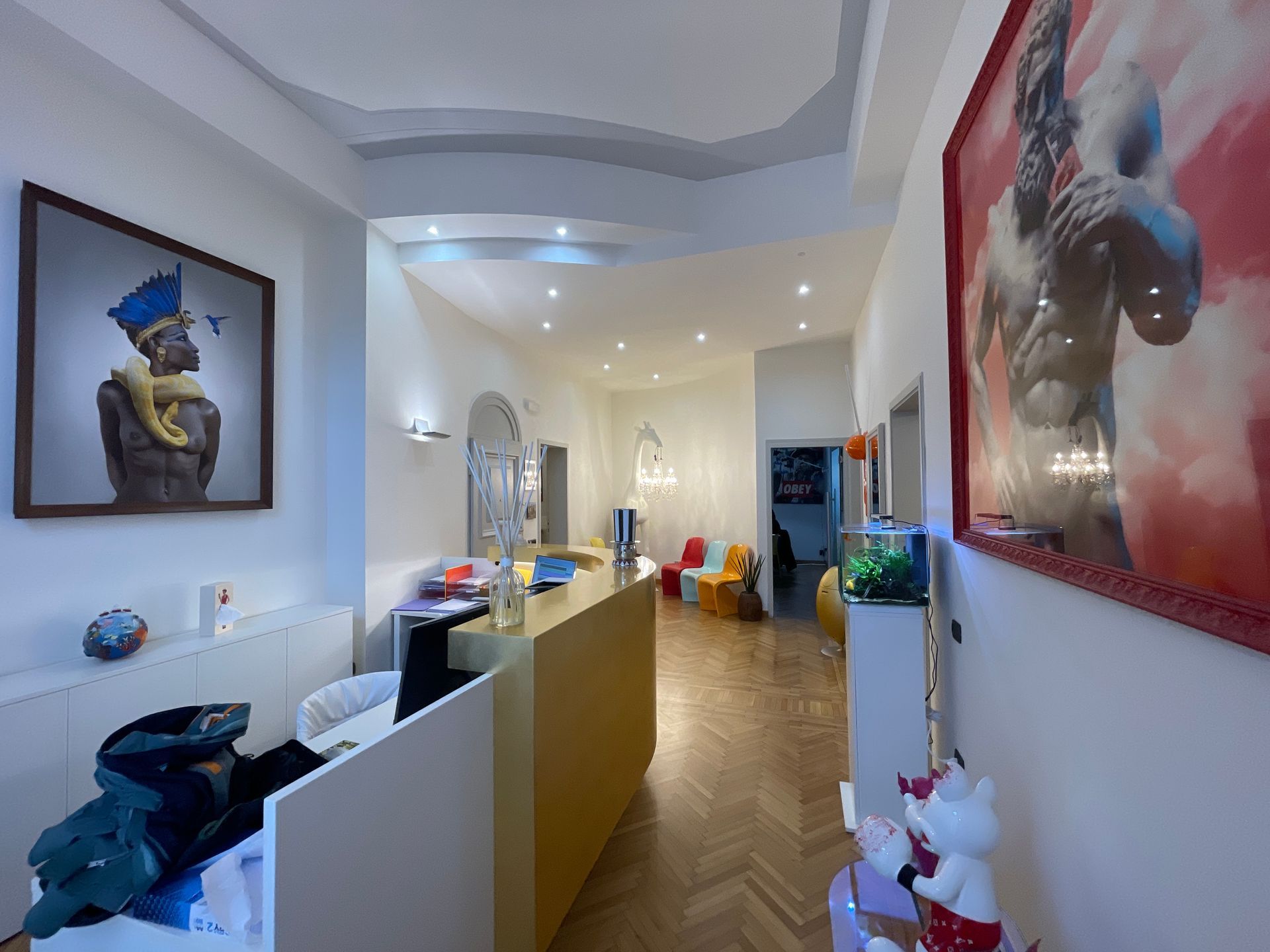 Area reception con opere d'arte, bancone giallo e sala d'attesa con sedie colorate.