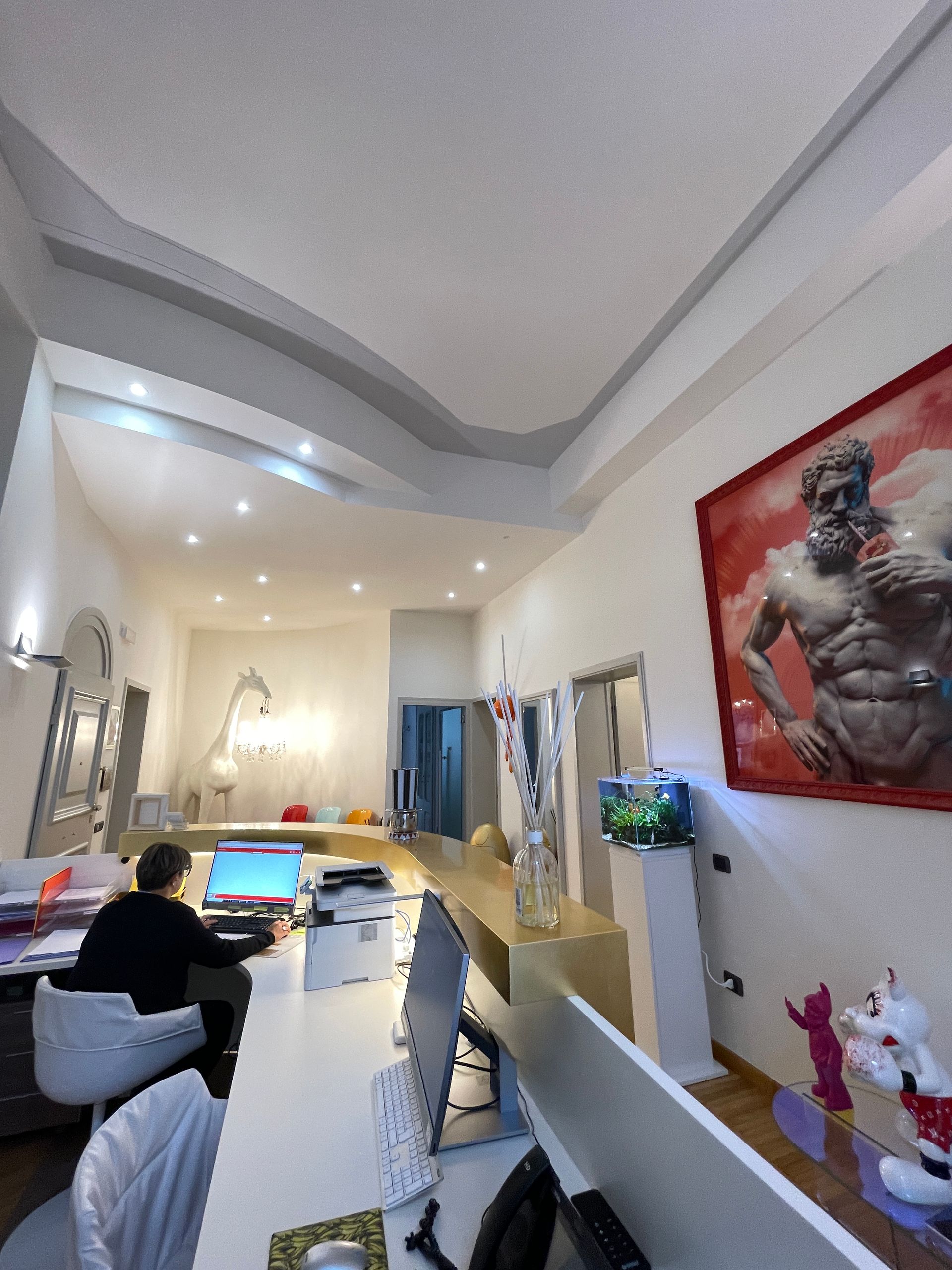 Una persona lavora a una scrivania in un ufficio ben illuminato, con opere d'arte e un acquario appesi alla parete.
