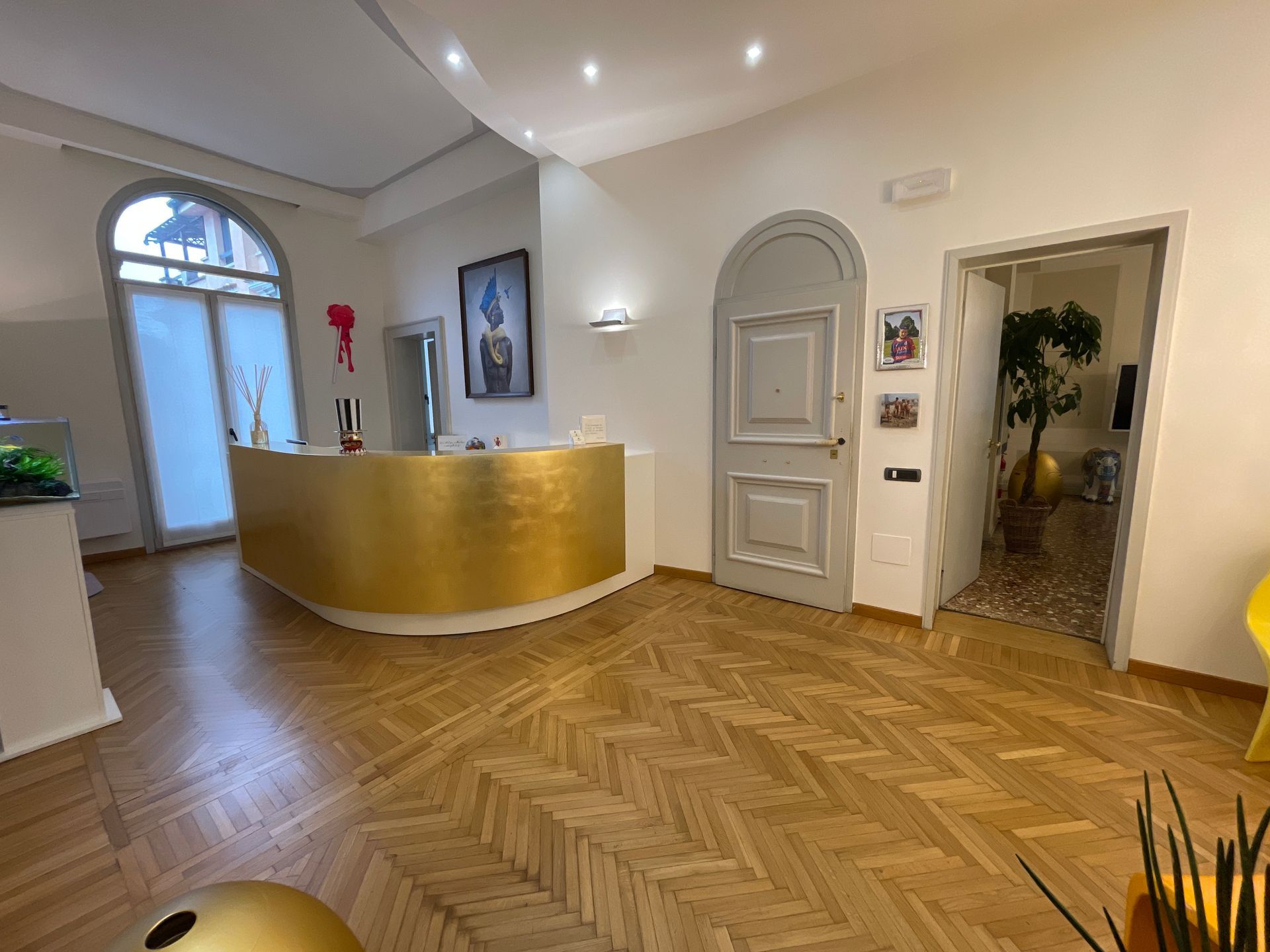 Area reception con scrivania curva color oro, pavimenti in legno e porta ad arco.