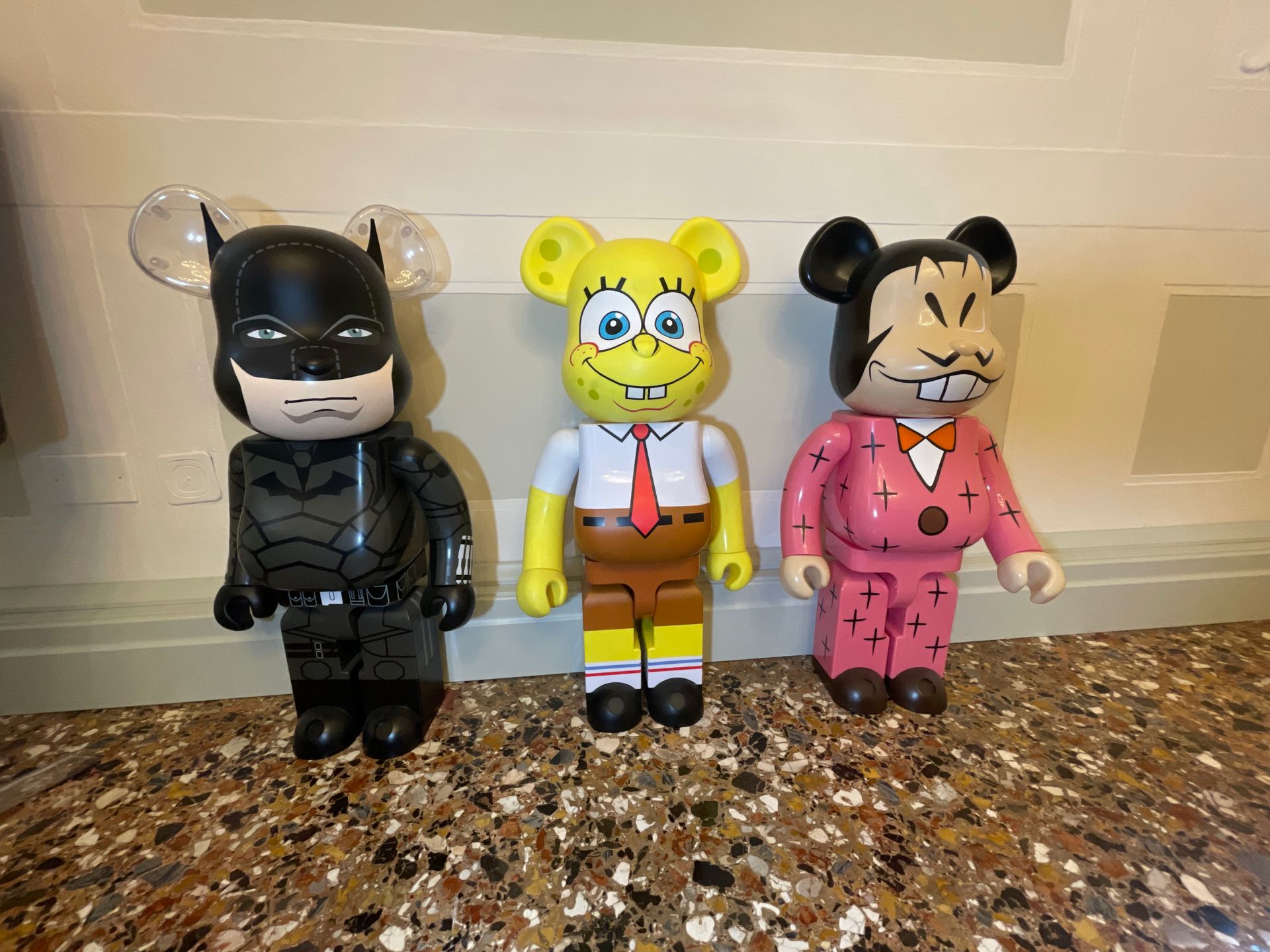 Tre statuette colorate a forma di orso: Batman, SpongeBob SquarePants e una statuetta rosa con un disegno cucito.