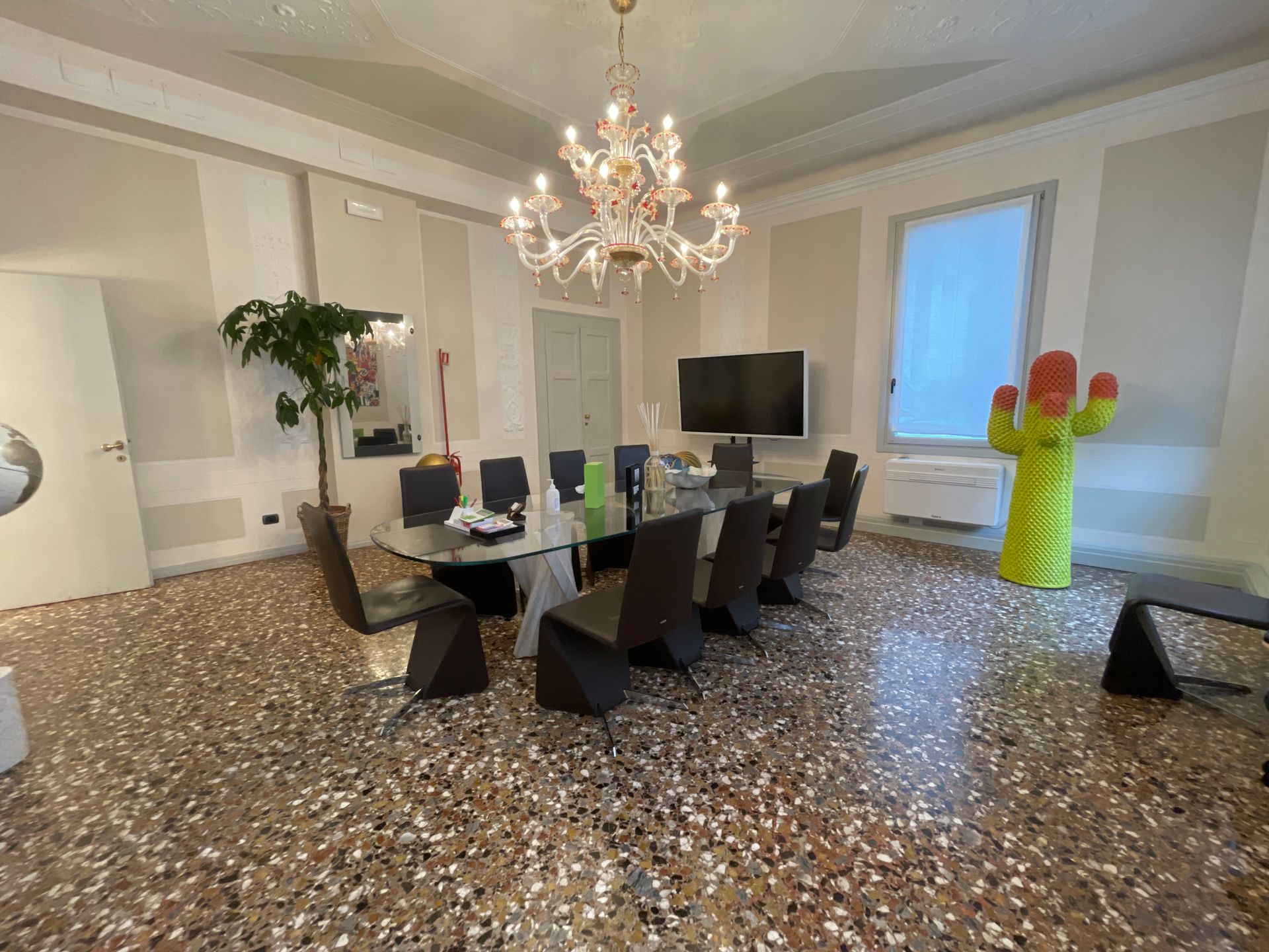 Sala conferenze con un grande tavolo, sedie, lampadario e una colorata scultura di cactus.