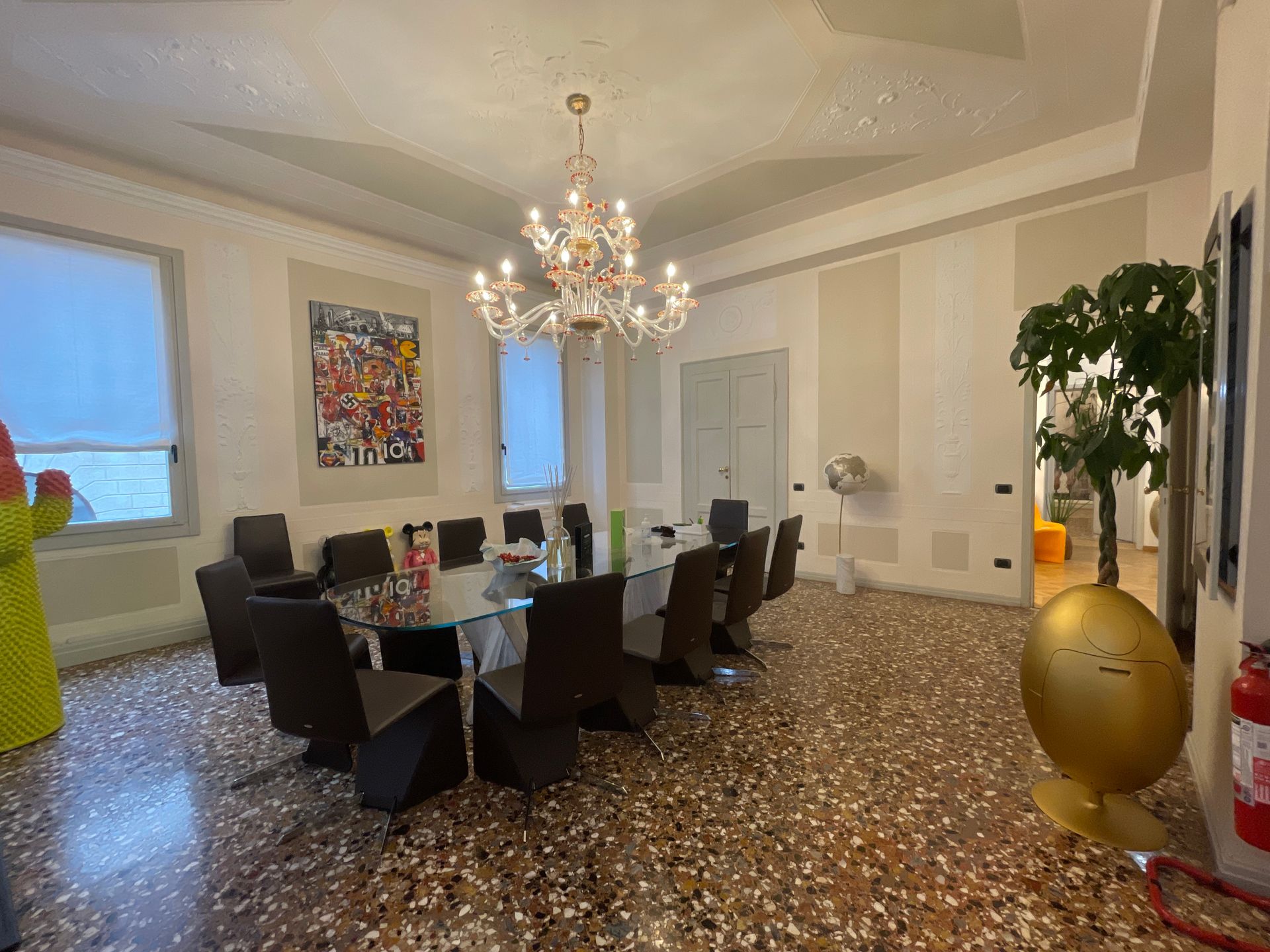 Sala conferenze con lungo tavolo in vetro, sedie, lampadario, opere d'arte e scultura a forma di uovo dorato.