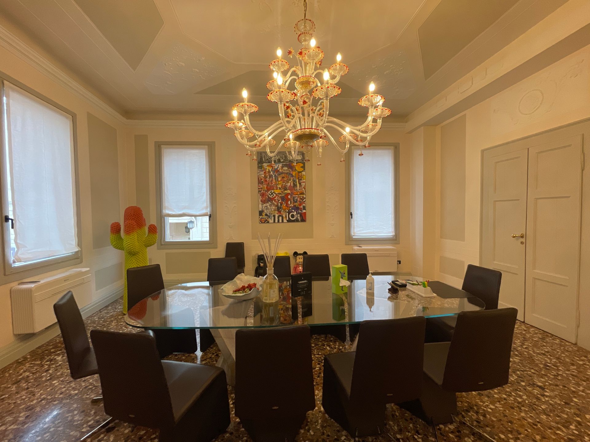 Elegante sala da pranzo con grande tavolo in vetro, sedie, lampadario, opere d'arte e finestre.