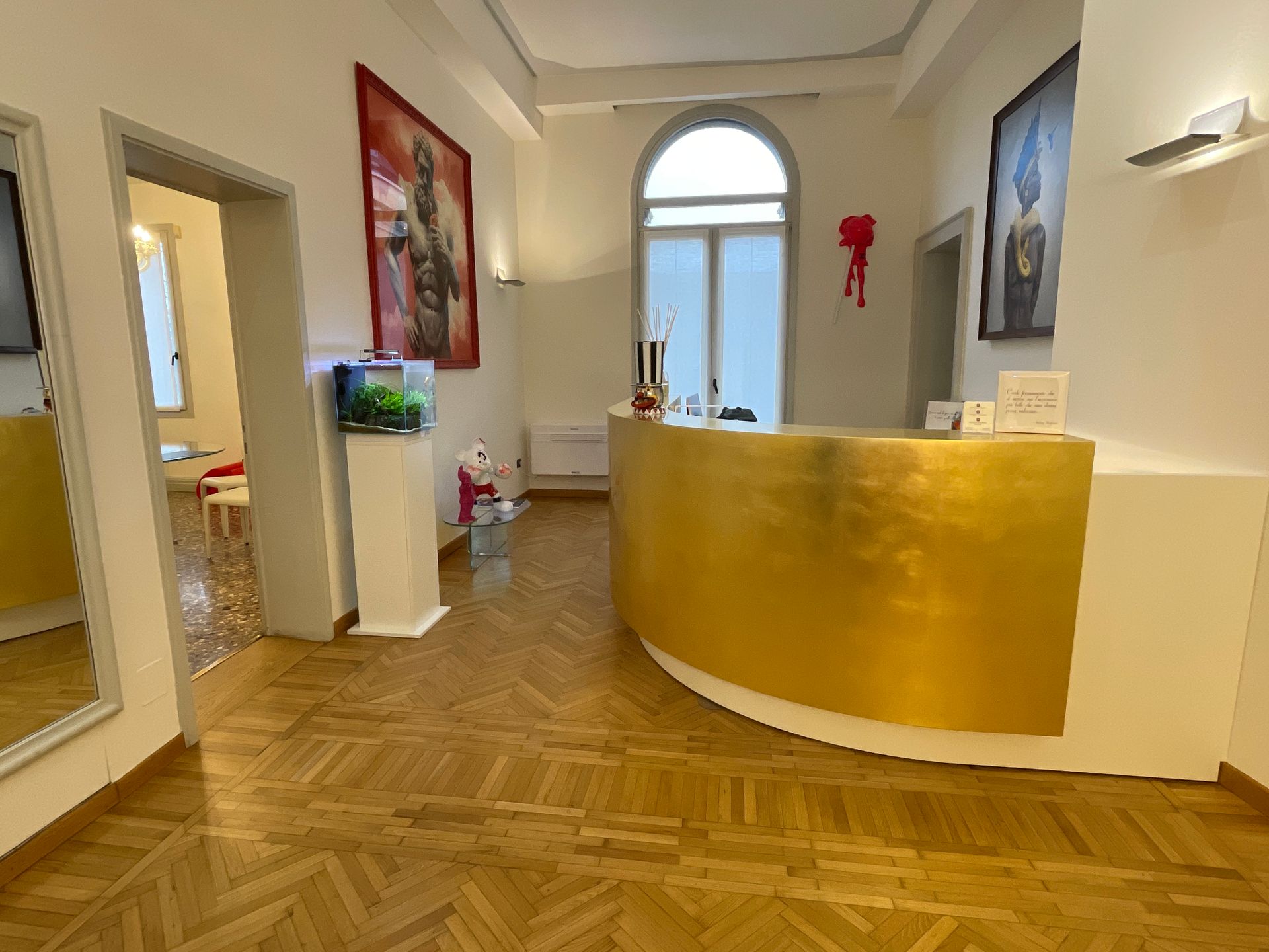 Area reception con bancone color oro, opere d'arte e acquario. Pavimenti in legno e finestra ad arco.