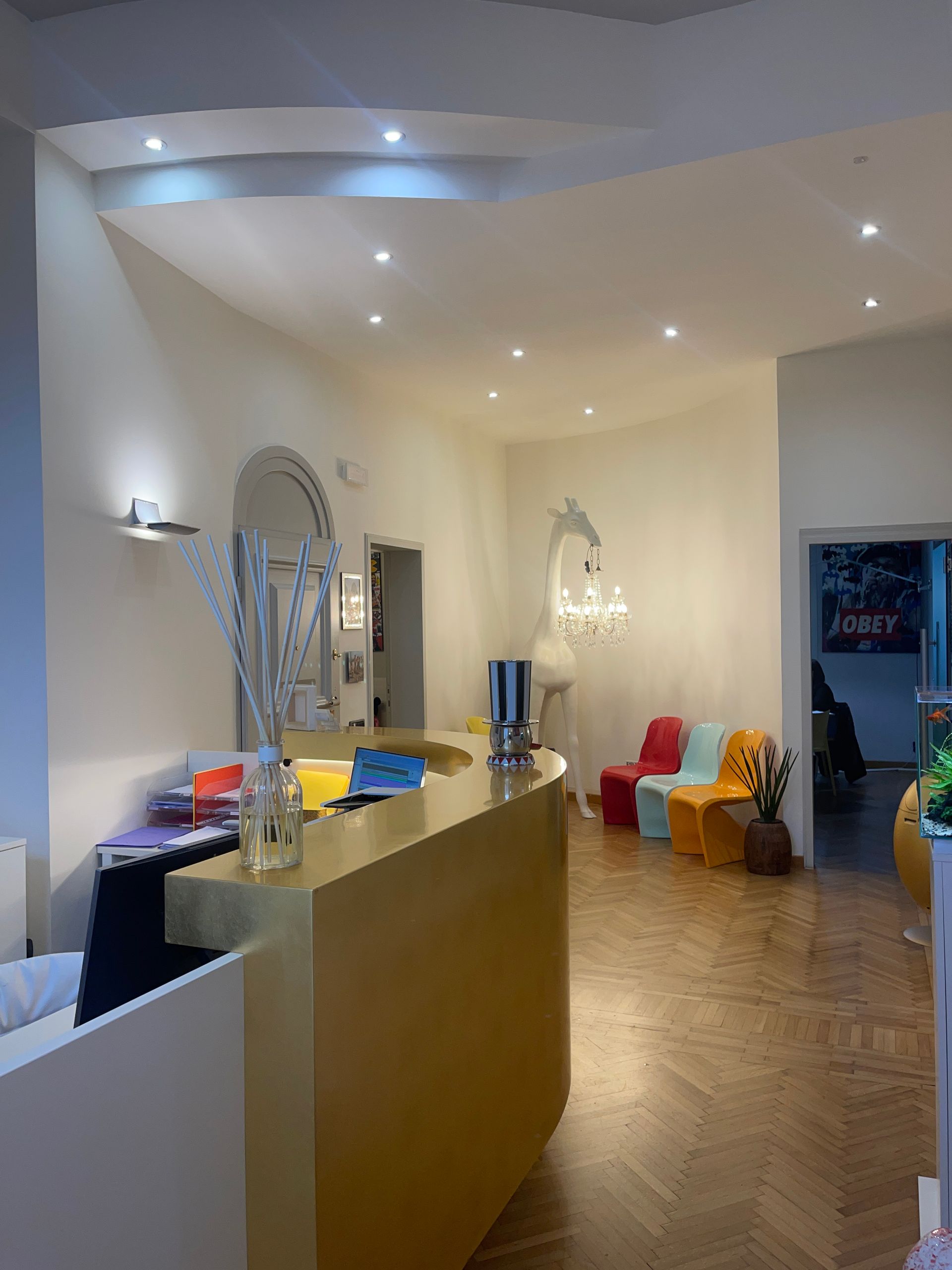 Area reception con bancone giallo, sedie colorate e lampadario.