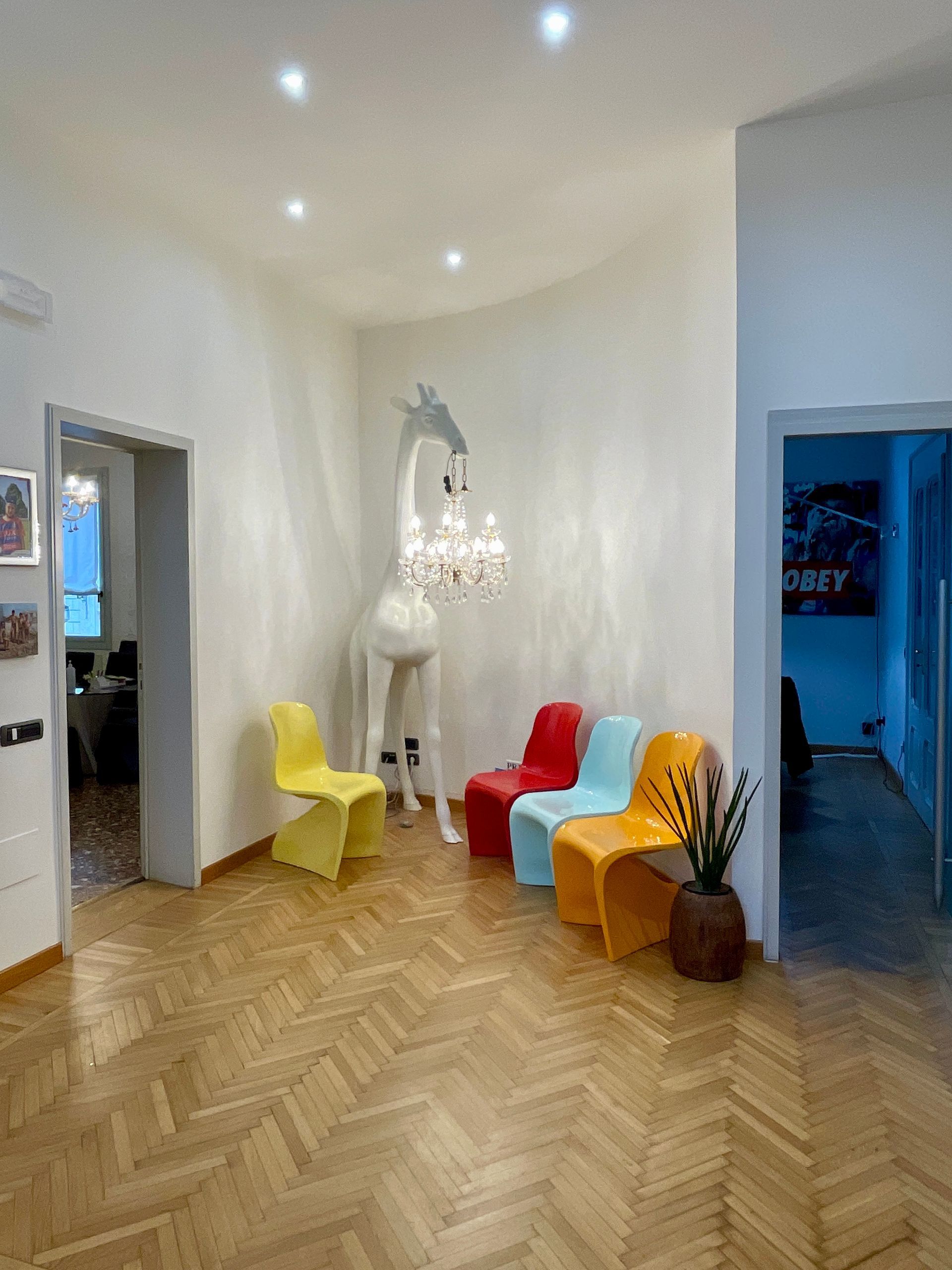 Un interno originale con sedie colorate, una lampada a forma di giraffa e pavimenti in legno.