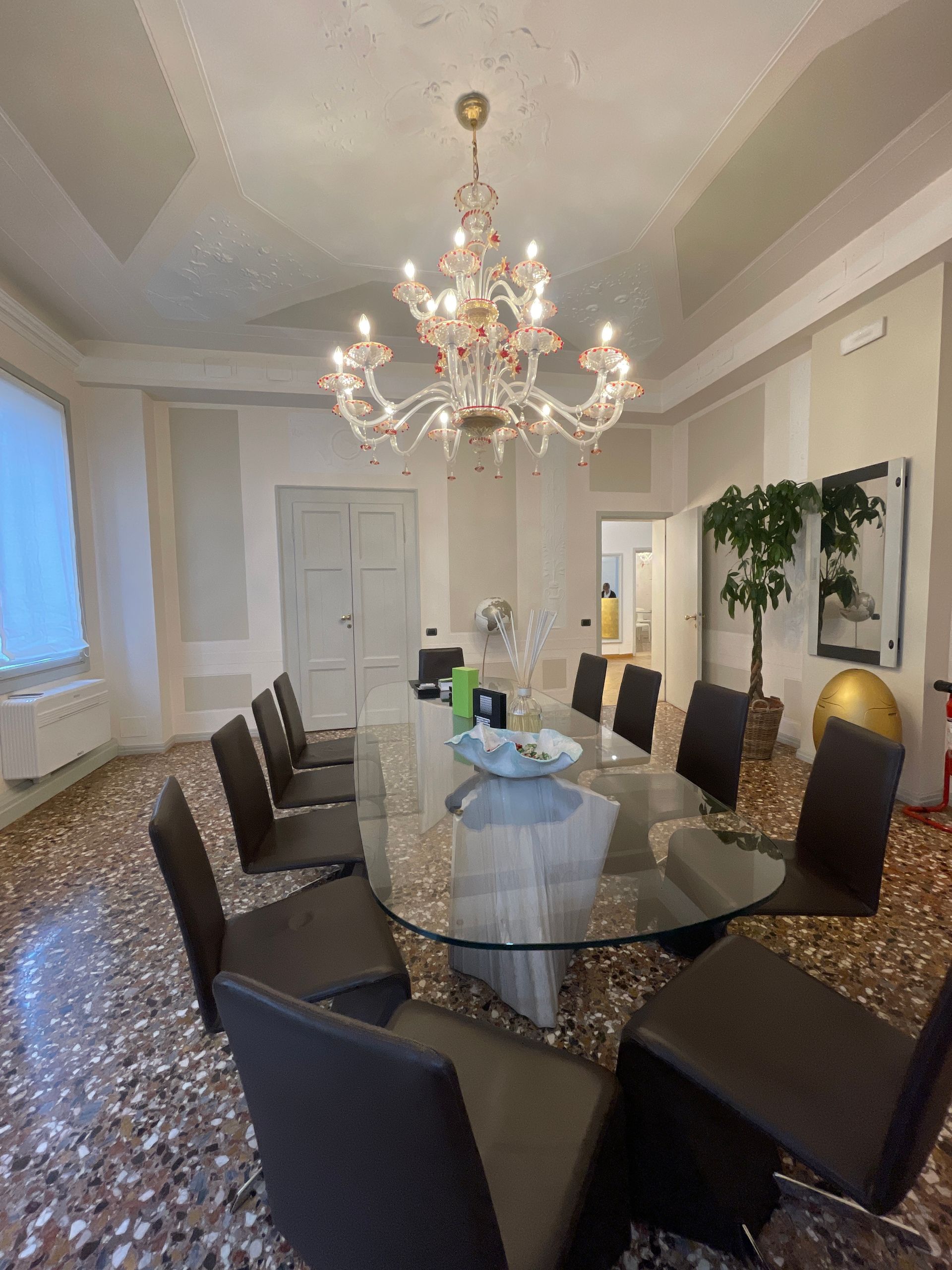 Sala da pranzo con un lungo tavolo di vetro, sedie e un lampadario decorato.