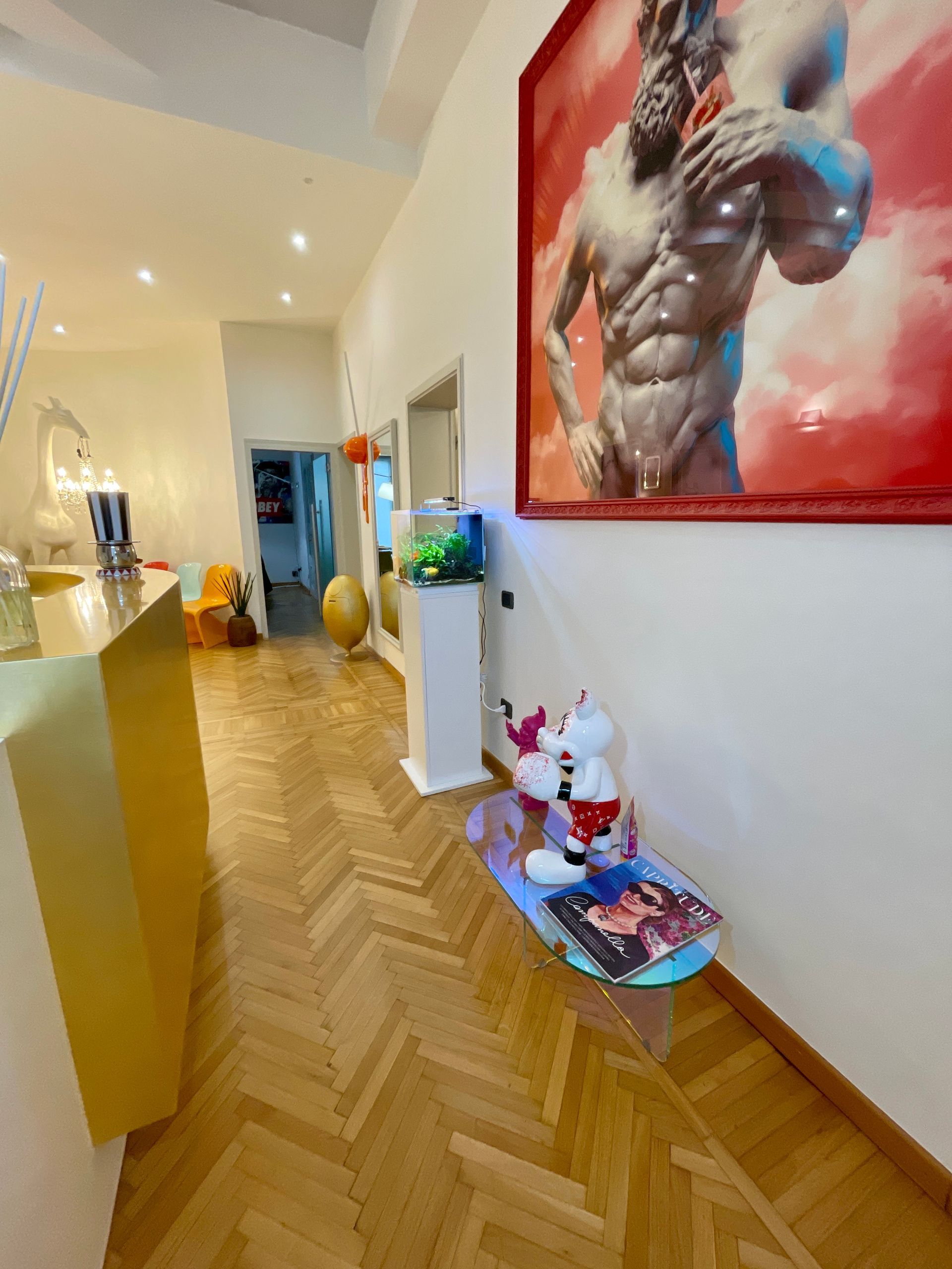 Corridoio con opere d'arte, acquario e bancone geometrico dorato; pavimento in legno.