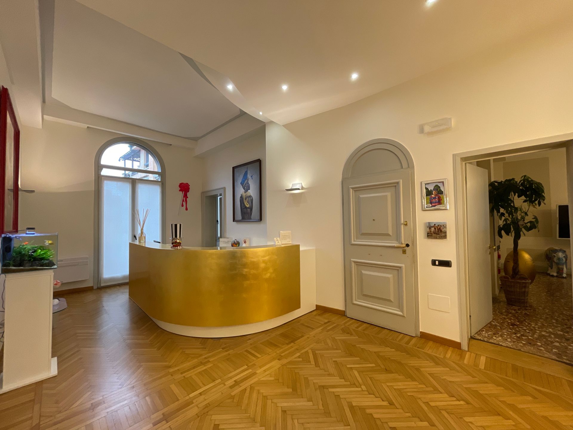 Area reception con bancone dorato, pavimenti in legno e porta aperta.