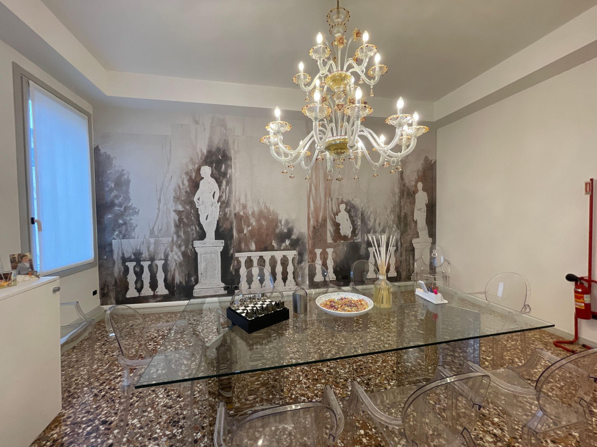 Sala da pranzo con tavolo in vetro, lampadario e un murale decorativo.