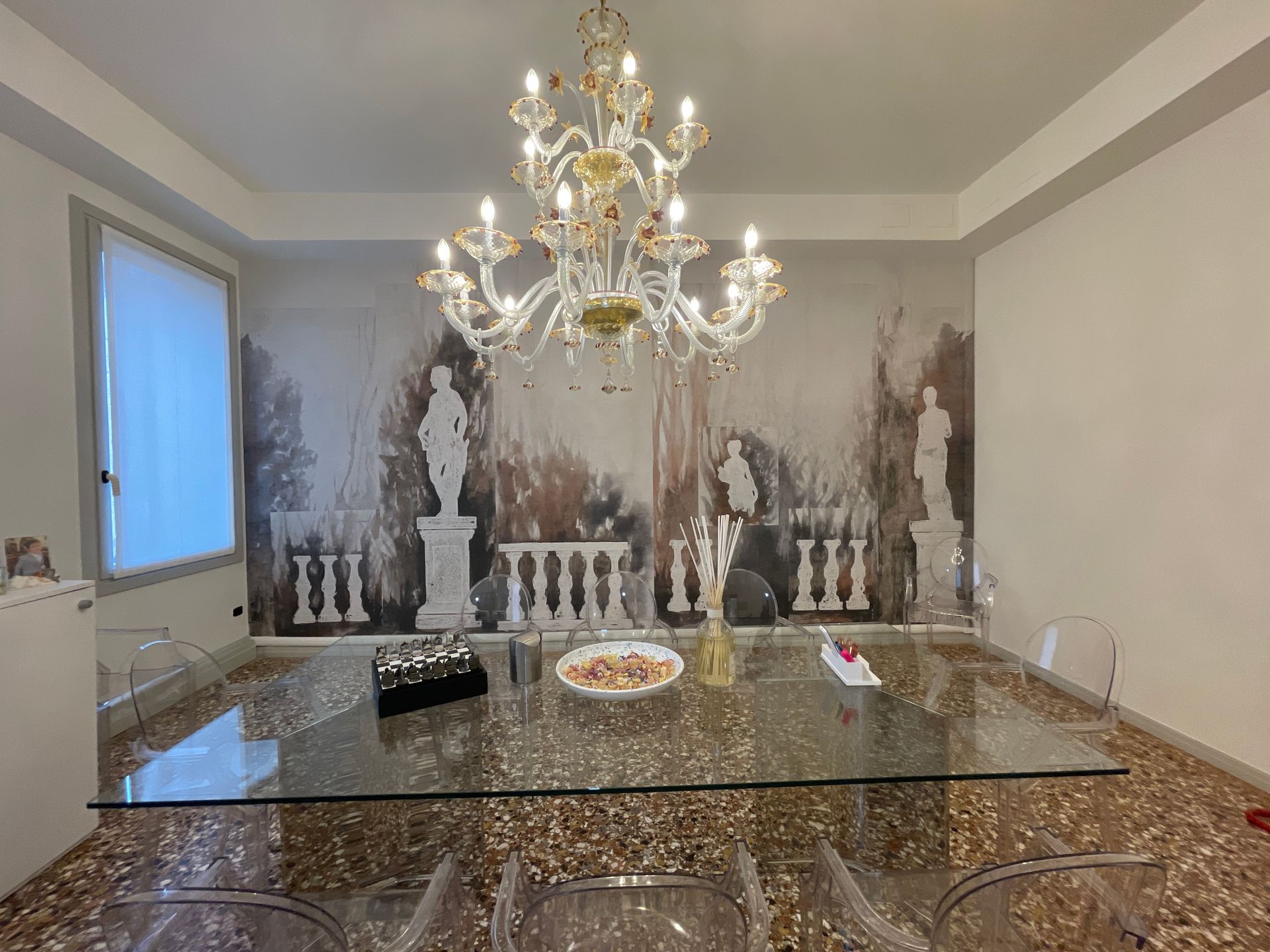Sala da pranzo con lampadario, tavolo in vetro e carta da parati raffigurante statue.