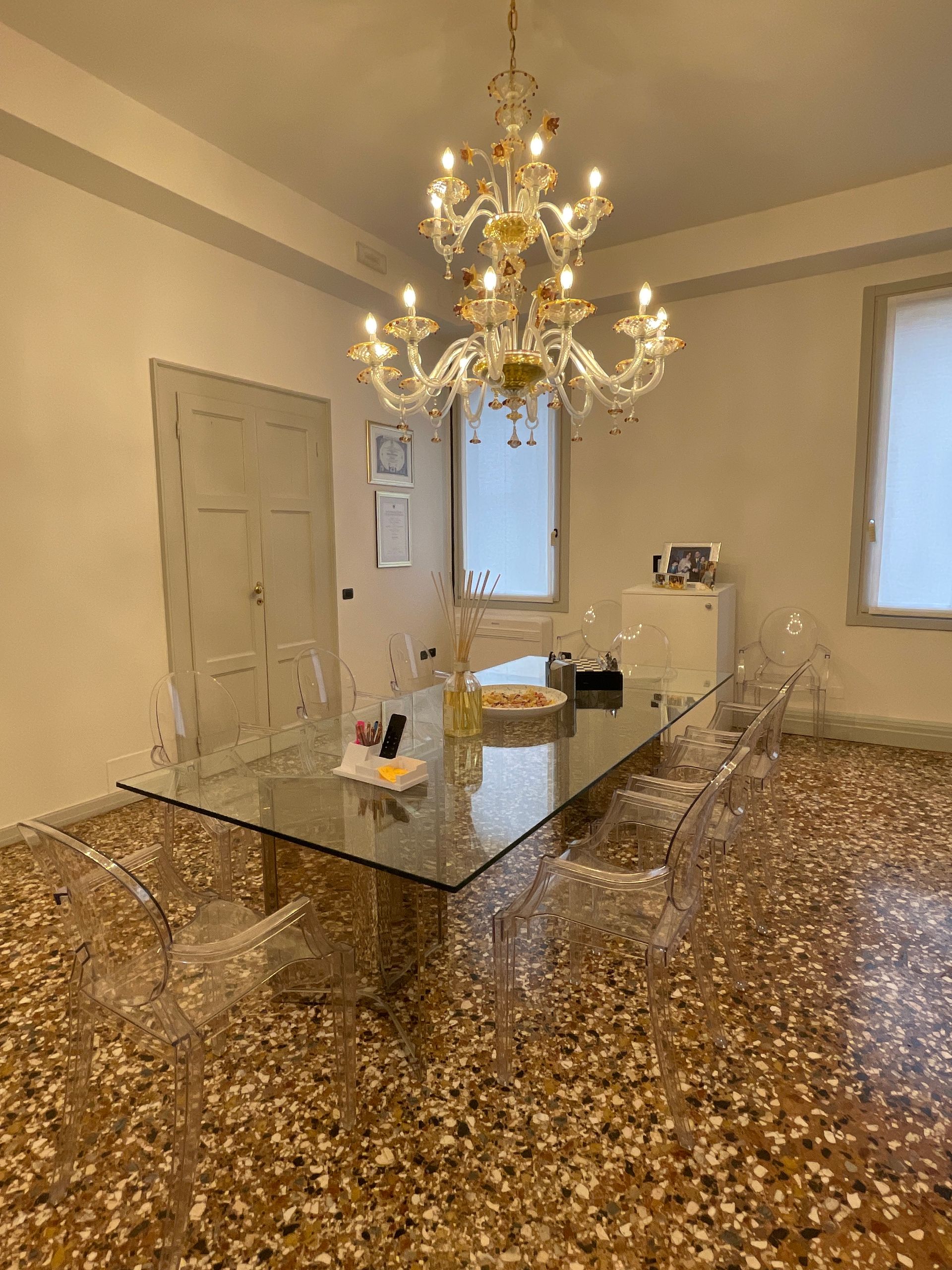 Sala da pranzo con tavolo trasparente, sedie, lampadario e pavimento in terrazzo.