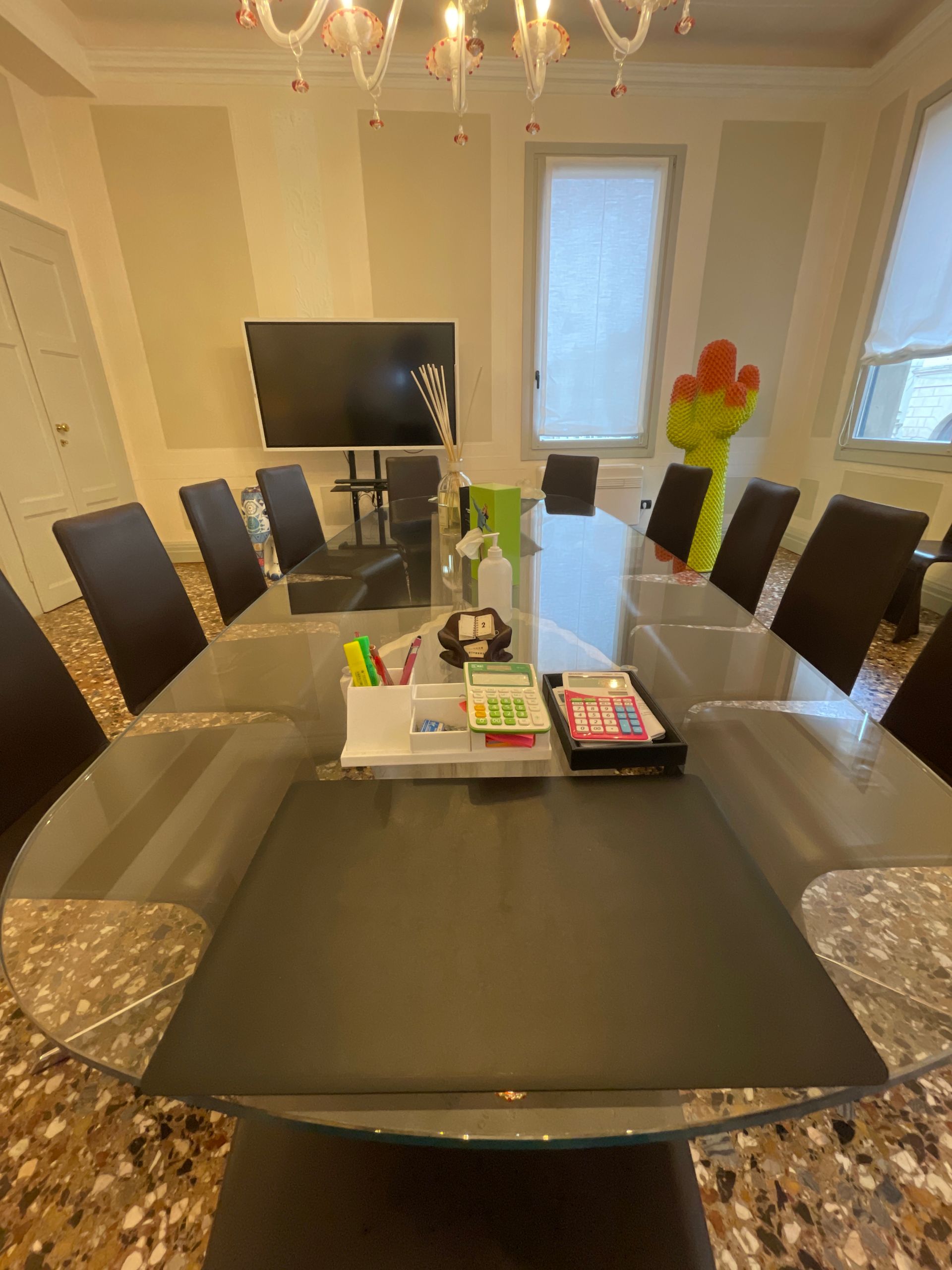 Una sala riunioni con un grande tavolo ovale in vetro, sedie e una TV. Le pareti sono chiare.