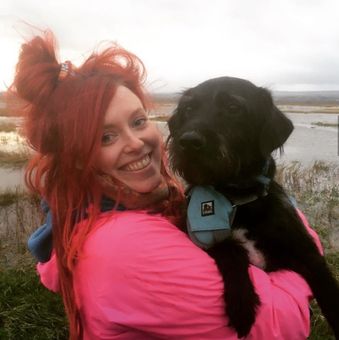 Dog Walker from Muddy Paws Adventures cuddling a black dog during a coastal walk near Neston