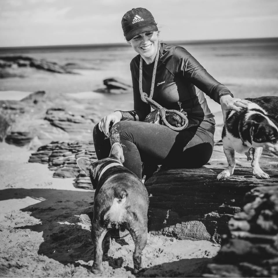 Dog walker sitting on the beach with a small dog enjoying a calm moment after a walk near Neston