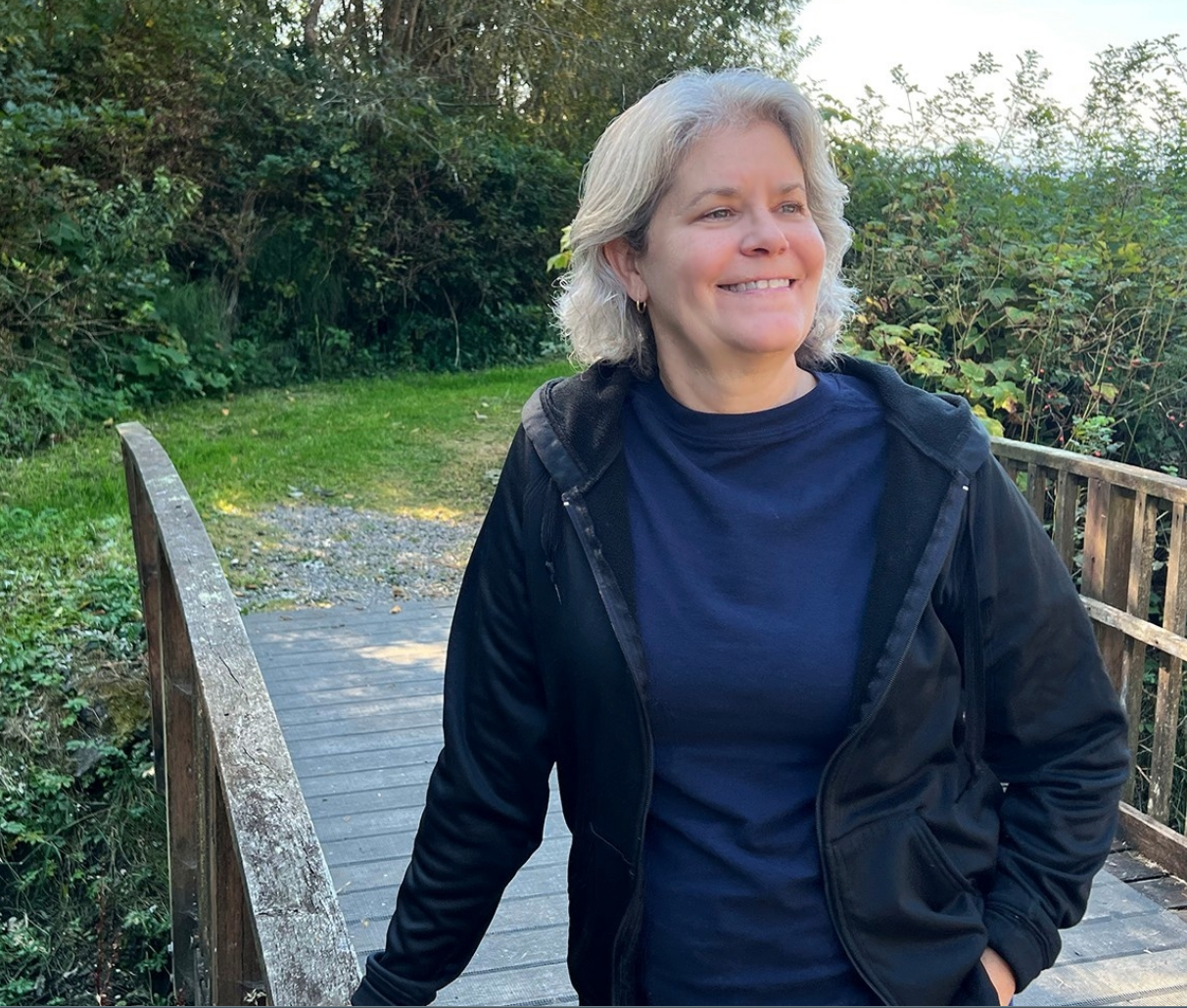 A woman in a black jacket is standing on a wooden bridge