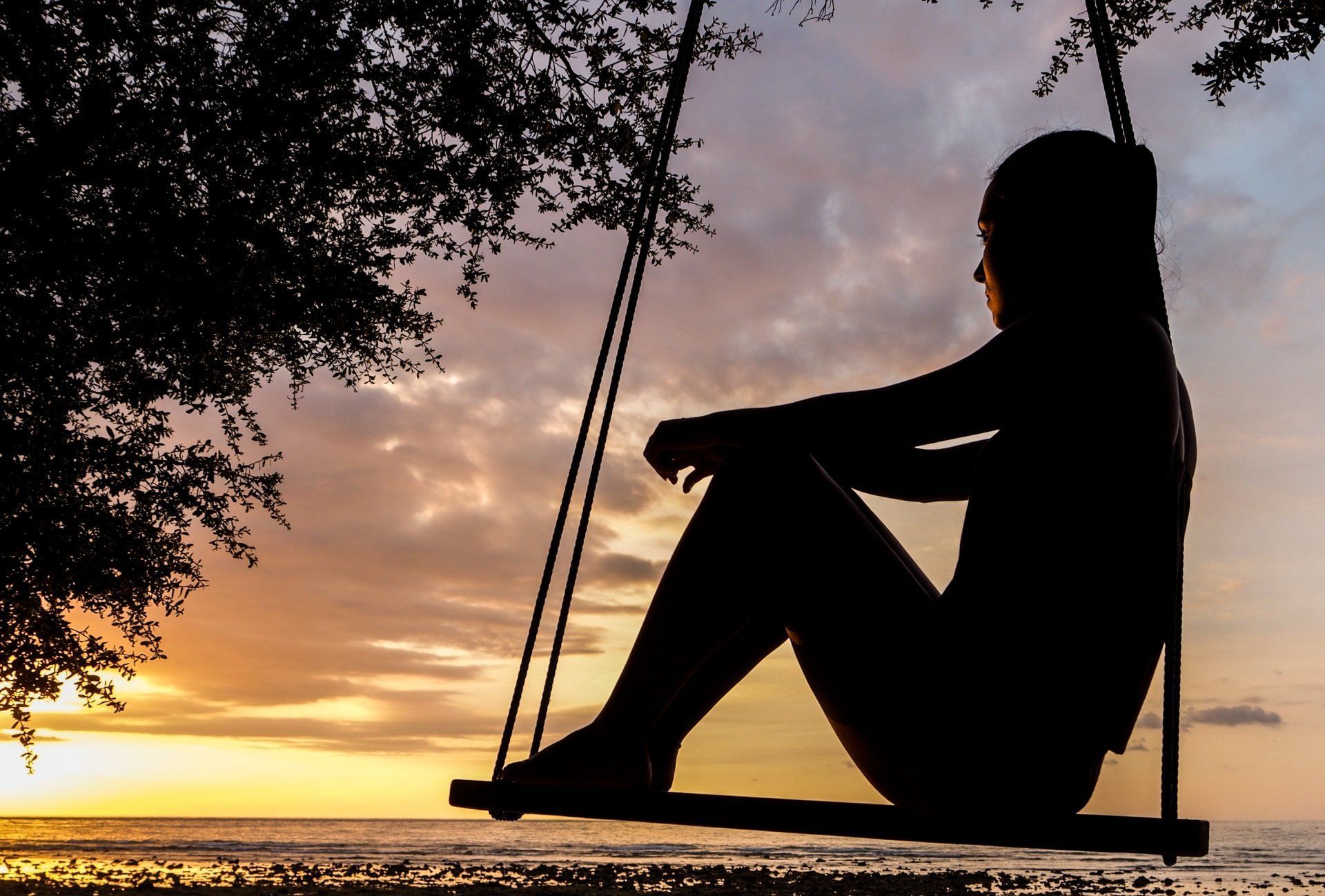 A silhouette of a woman sitting on a swing at sunset.