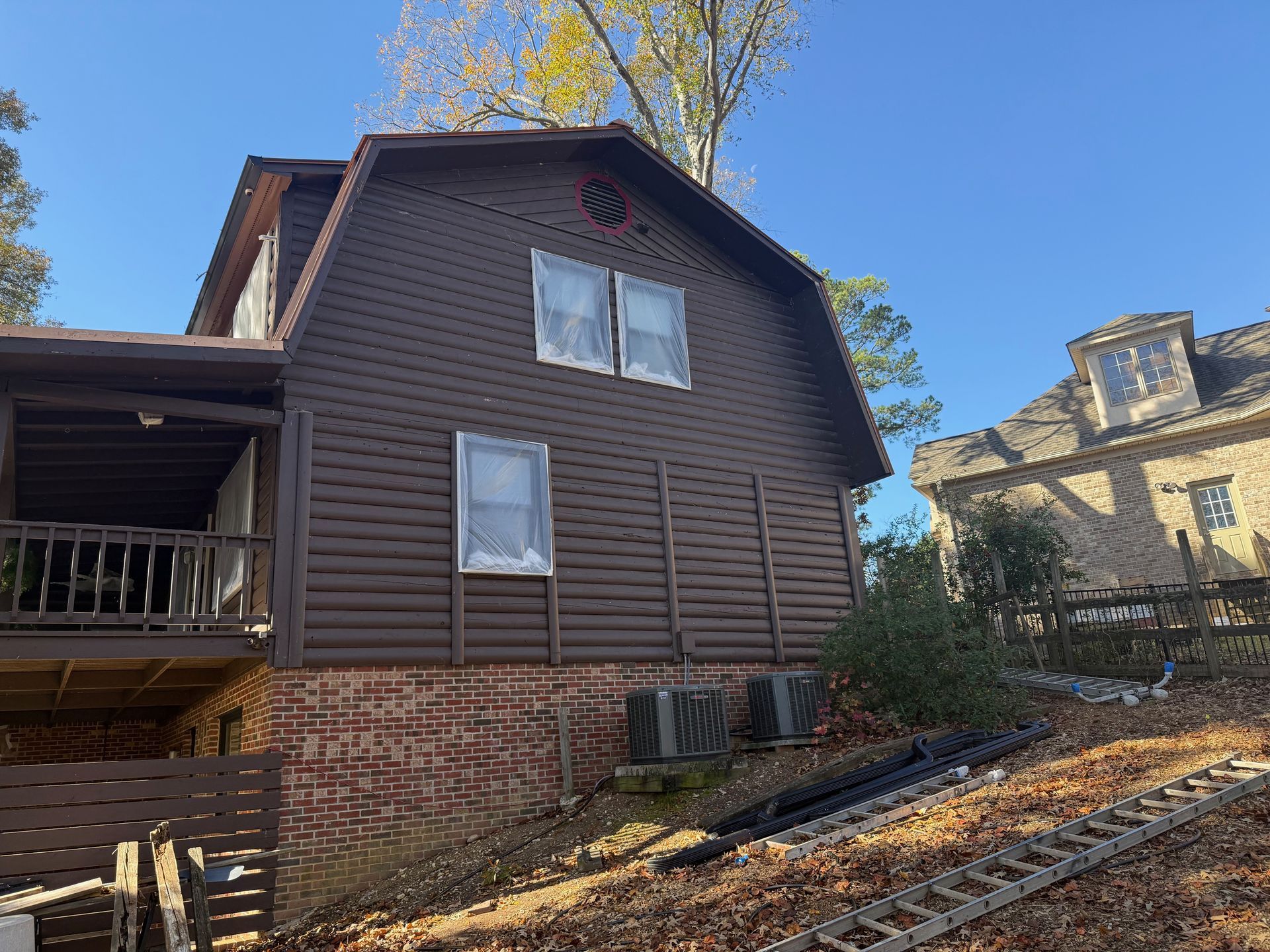 Brown house with arched roof, two rows of windows, brick foundation, and a deck.