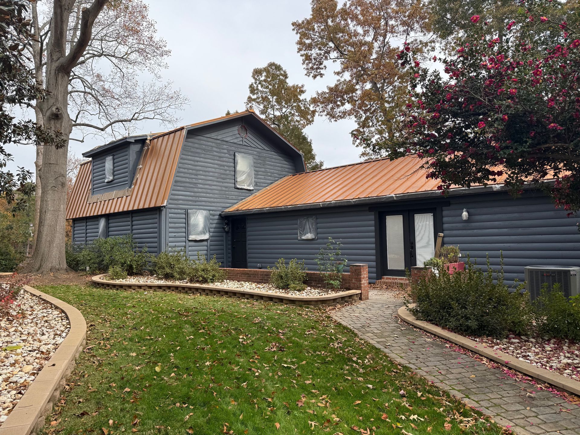 Gray house with orange roof, surrounded by trees and a brick pathway.