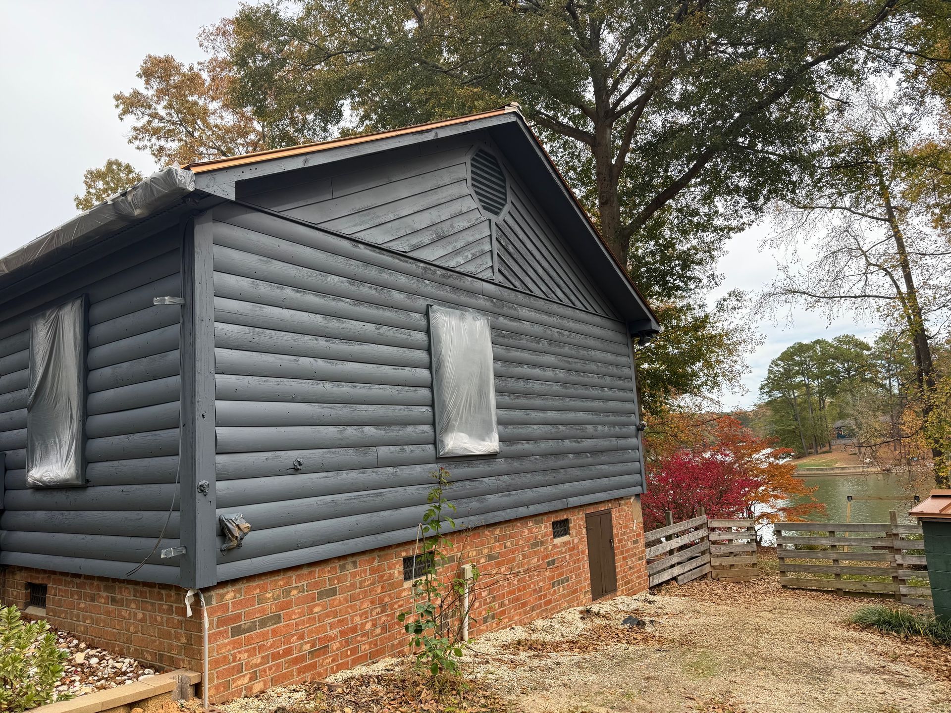 Dark gray building with brick base, boarded up windows, and a circular vent, surrounded by trees.