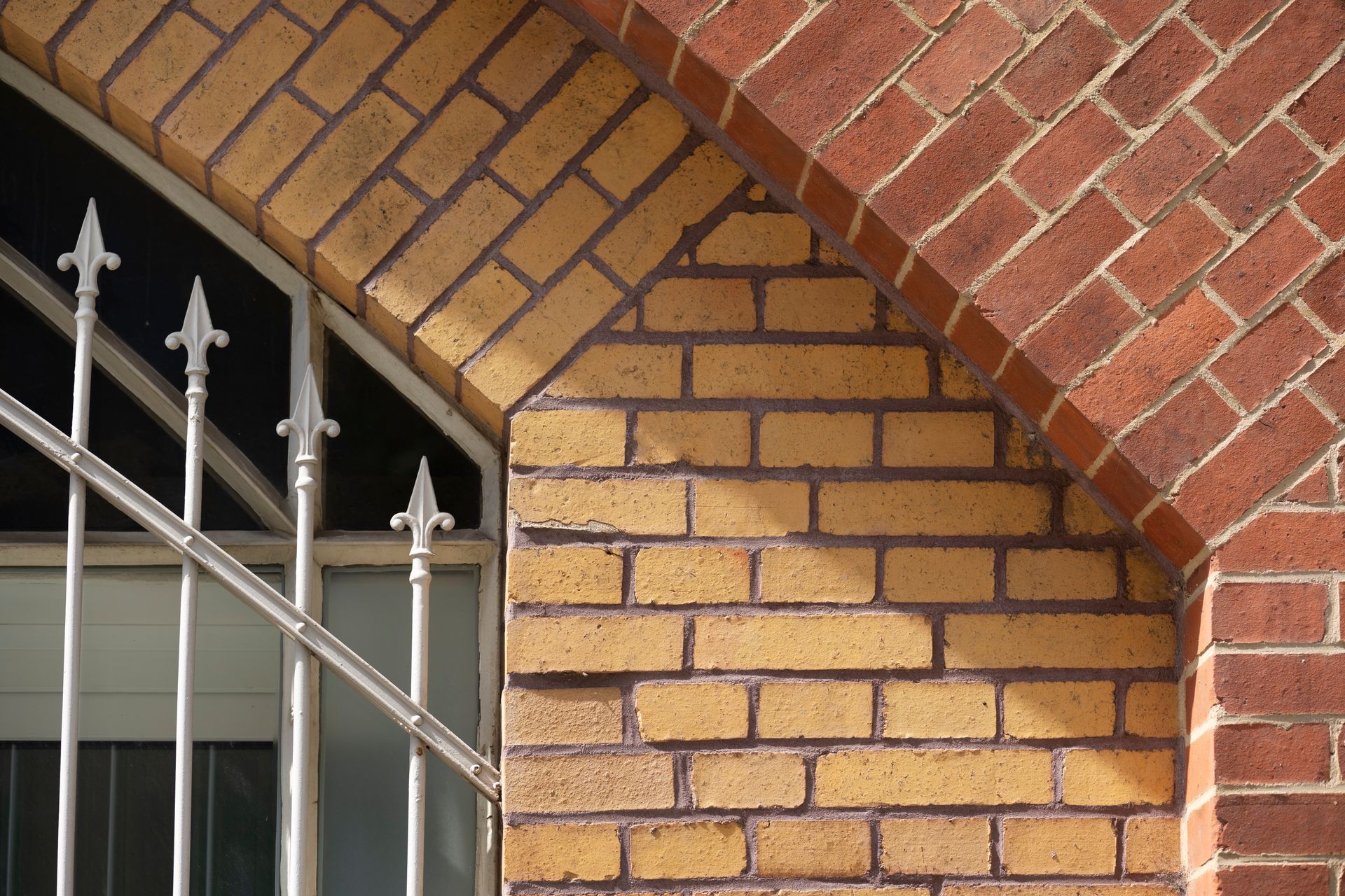 Brick wall with arched window frame and ornate iron bars.
