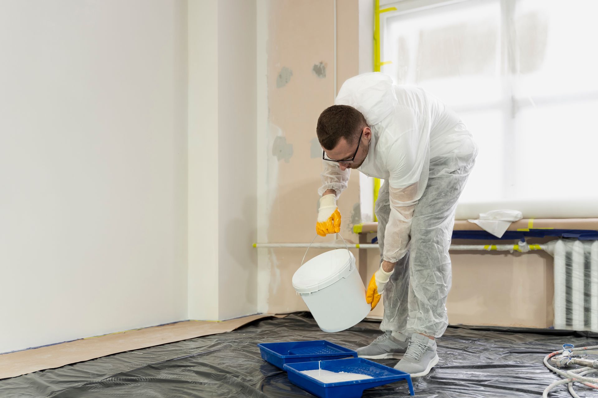 A person in protective gear pouring paint into a tray, preparing to paint a room.