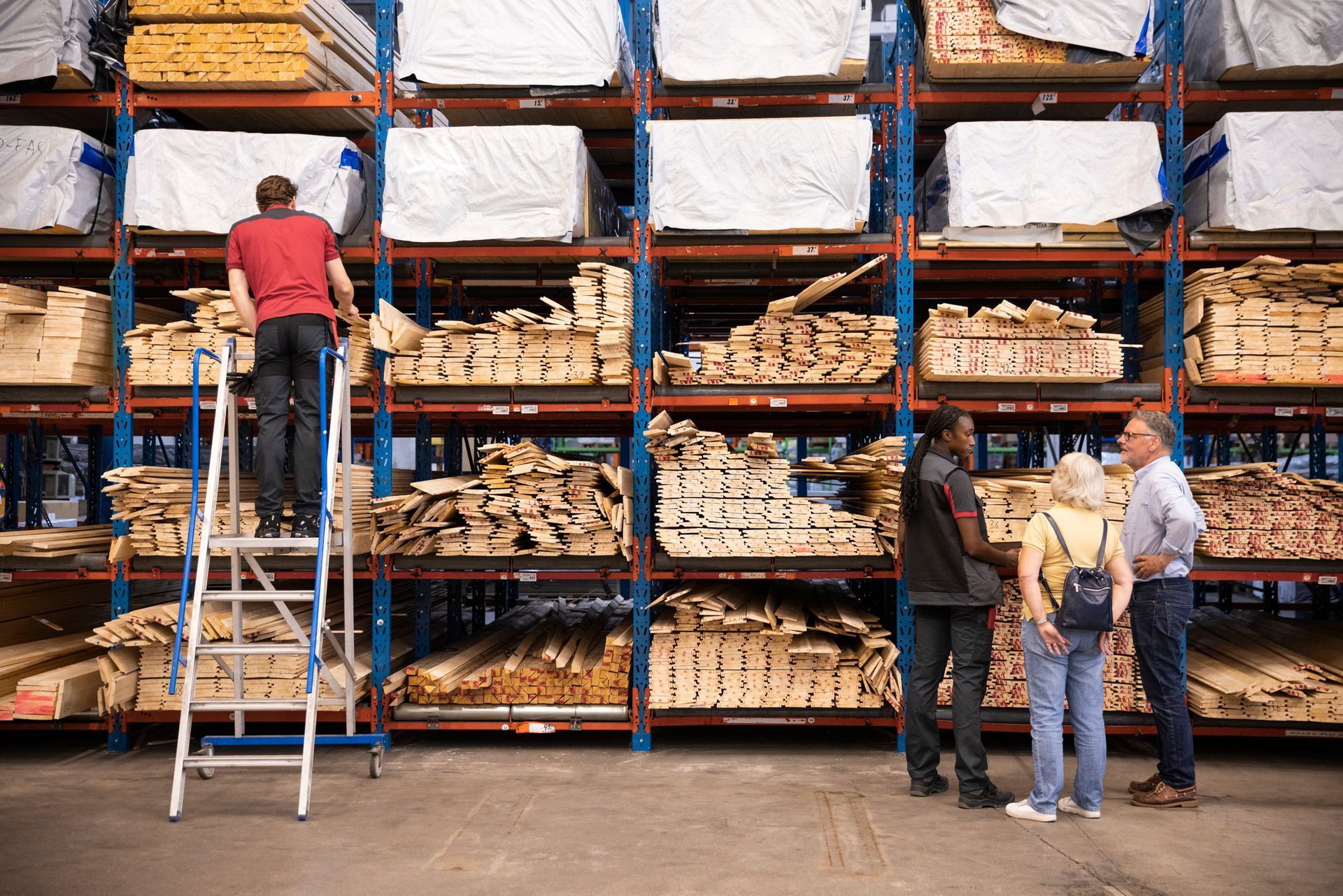 Saleswoman helps customers as a salesman retrieves lumber products from a high shelf in the store.