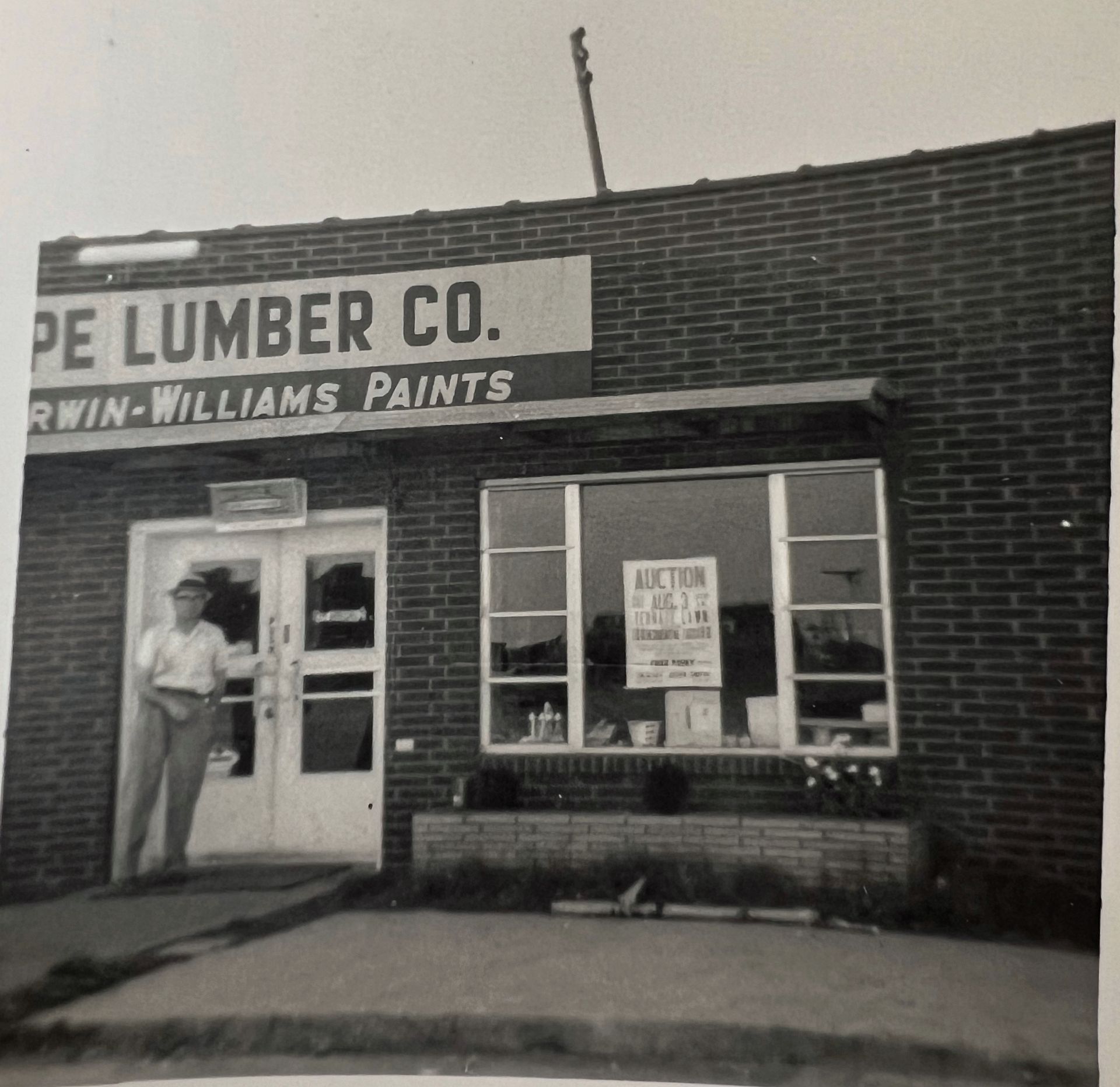 A man stands in the doorway of a brick building labeled 