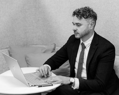 A man in a suit and tie is sitting at a table using a laptop computer.